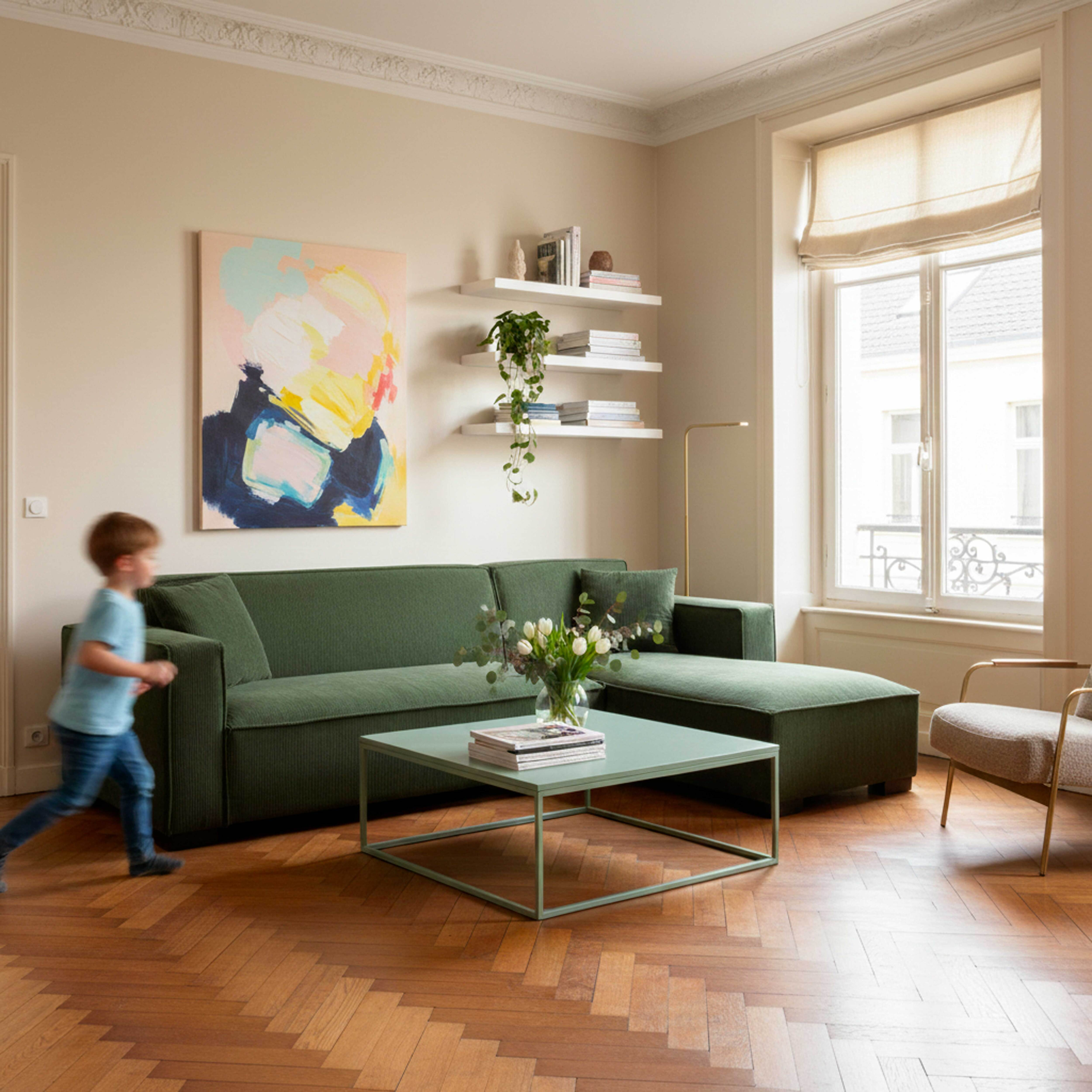 Ein Kind rennt an einem grünen Sofa in einem Wohnzimmer vorbei. Es gibt ein Gemälde und ein Fenster.