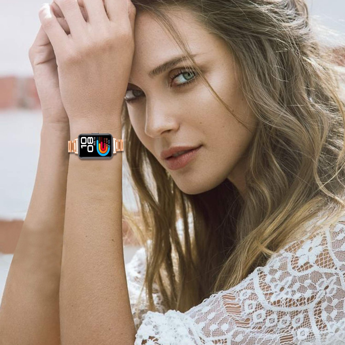 Eine Frau mit grünen Augen trägt eine Smartwatch. Sie hat helle Haut, lange wellige Haare und ein weißes Spitzentop. Sie schaut in die Kamera.