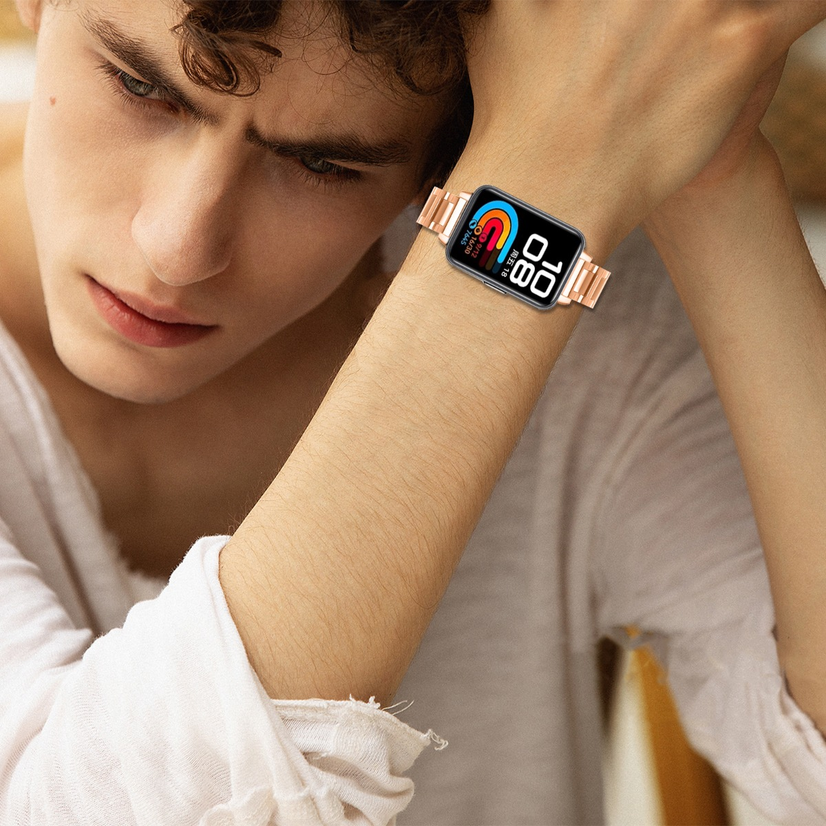 Eine Person trägt eine roségoldene Smartwatch am Handgelenk. Die Uhr zeigt die Uhrzeit und andere Daten an. Die Person schaut nach unten.