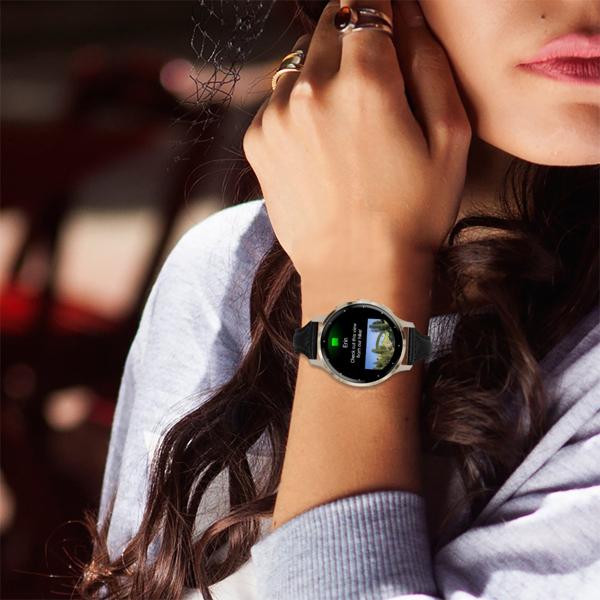 Muñeca de mujer con reloj inteligente mostrando un mensaje. Su mano toca su rostro, anillos visibles.