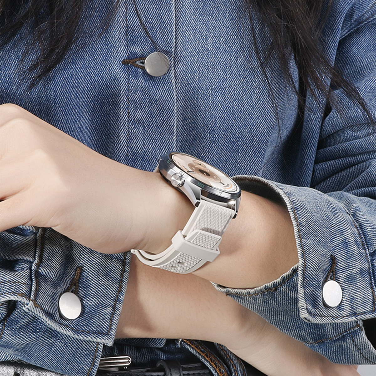 Una persona che indossa uno smartwatch argentato con cinturino bianco. Indossa una giacca di jeans. L'orologio mostra l'ora.