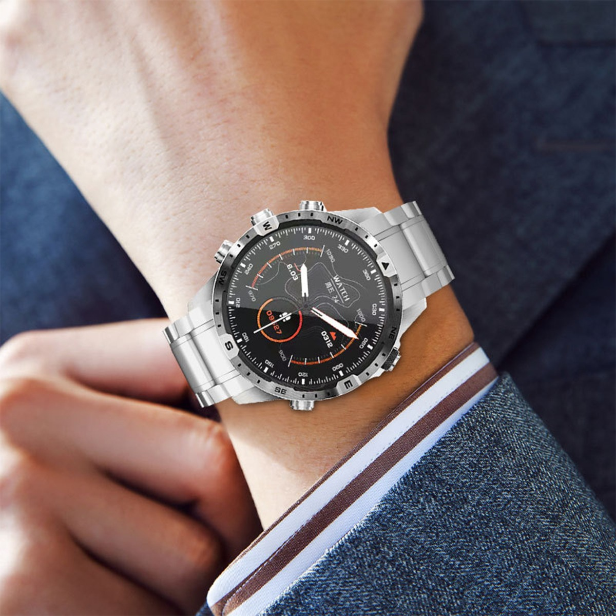 Il polso di una persona con uno smartwatch argentato. L'orologio visualizza l'ora, la data e altre metriche. La persona indossa un abito grigio.