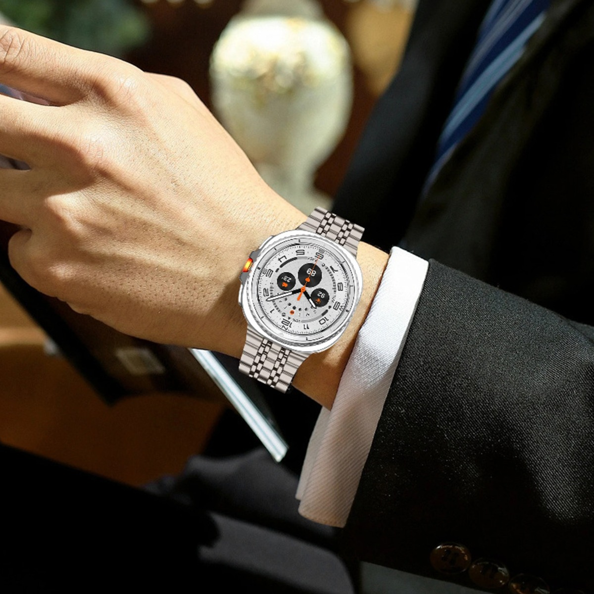 Polso di un uomo con un orologio da polso argentato. L'orologio ha un quadrante bianco, quadranti neri e un accento arancione. L'uomo indossa un abito.