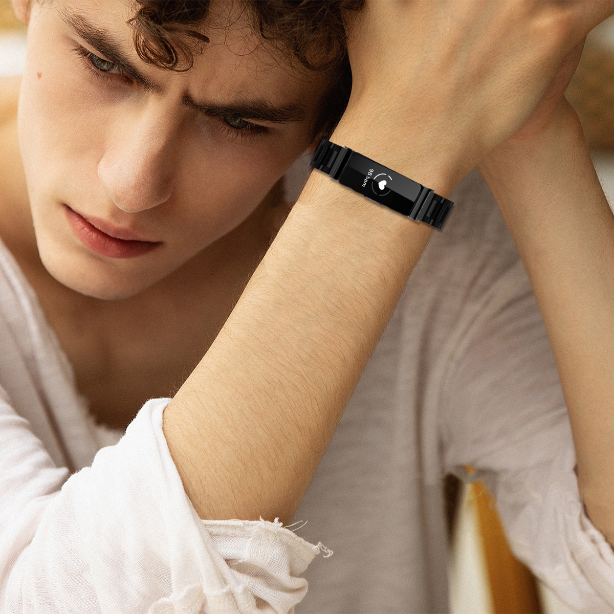 Ein Mann mit einer schwarzen Smartwatch. Er trägt ein weißes Hemd und stützt seinen Kopf auf seinen Arm.