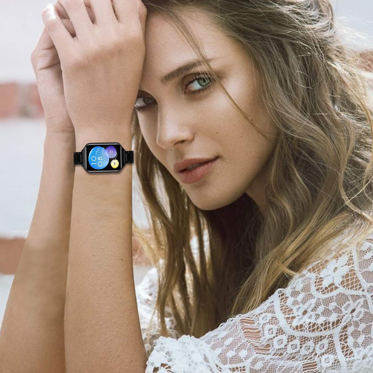Una mujer con cabello largo y un top de encaje blanco lleva un reloj inteligente. La esfera muestra la hora y la fecha.