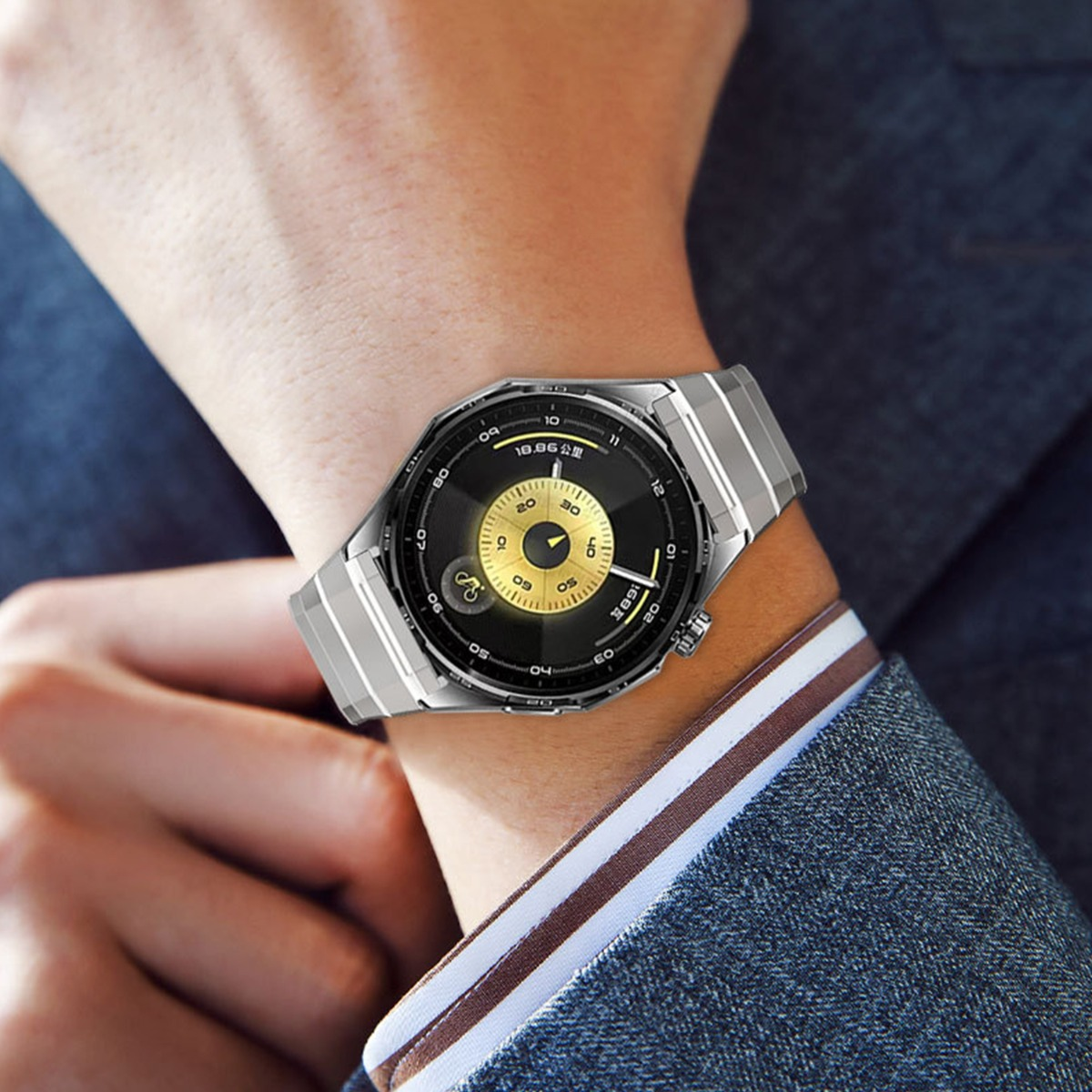 Una persona que lleva un reloj inteligente plateado con pantalla negra y detalles dorados en la muñeca. El fondo es un traje.