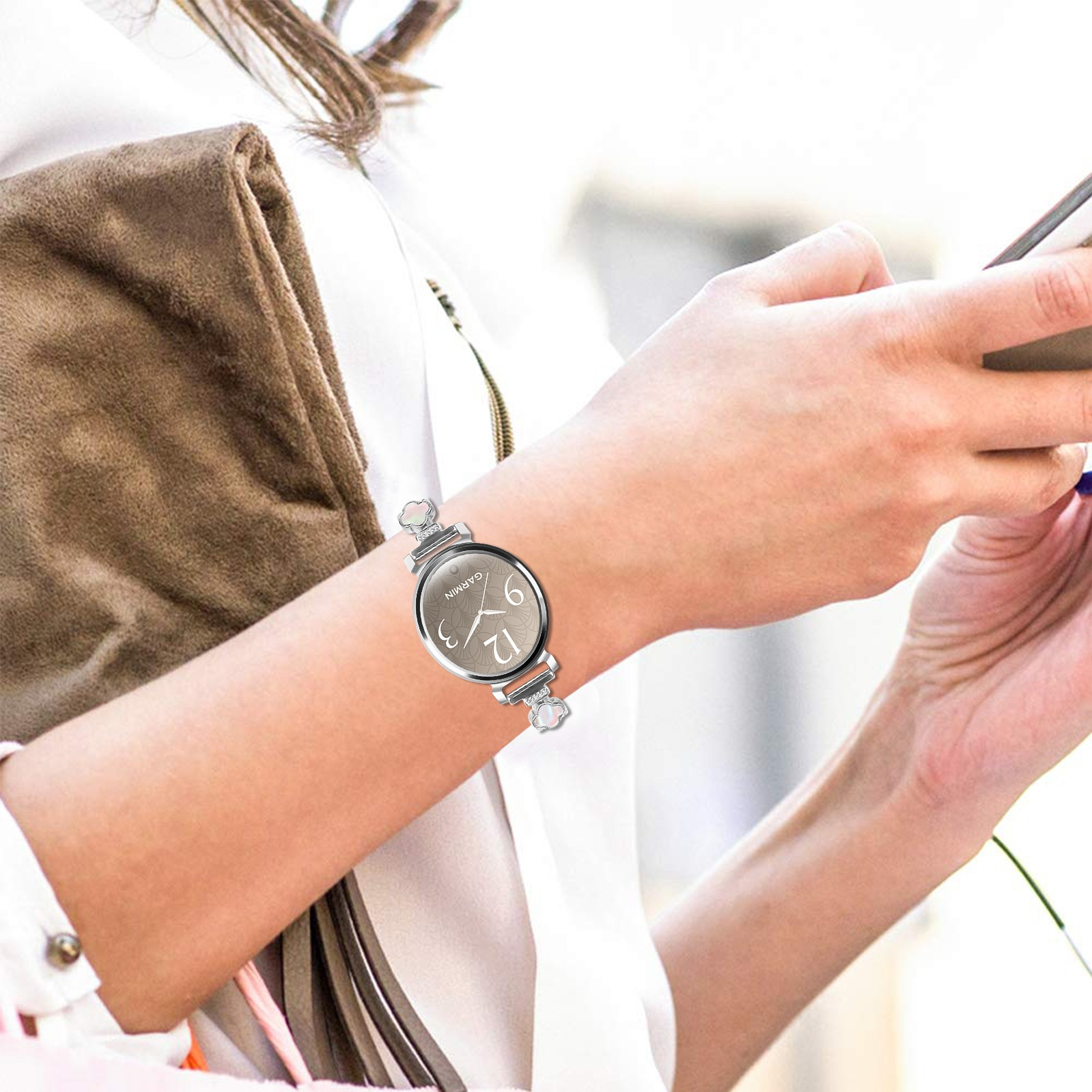 Eine Person mit einer Uhr und einer braunen Handtasche. Sie hält ein Telefon.