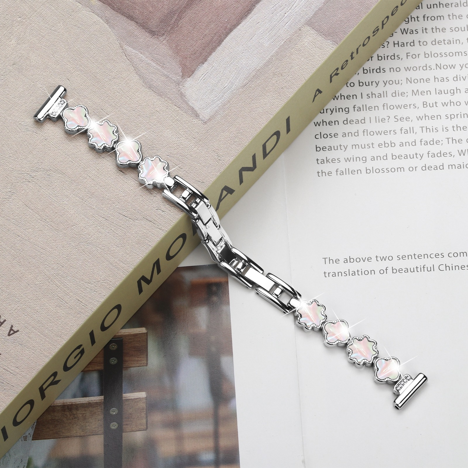 Ein silbernes Armband mit blütenförmigen Gliedern liegt auf einem Buch. Text ist auf dem Buch sichtbar.