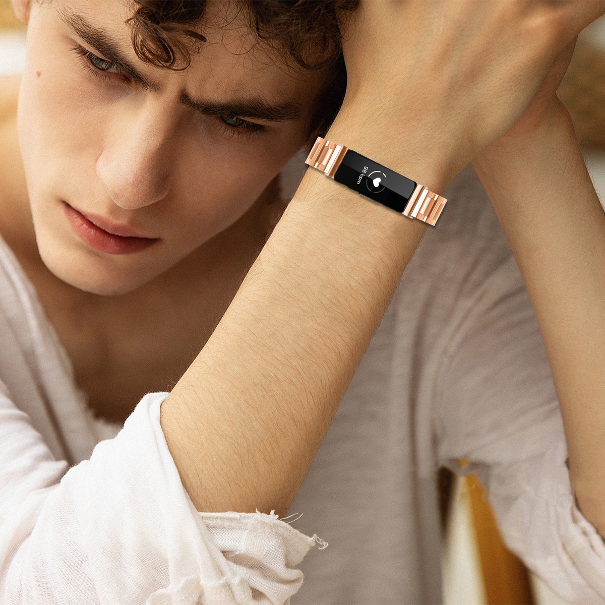 Ein Mann trägt eine roségoldene Smartwatch. Er trägt ein weißes Hemd und stützt seinen Kopf auf seine Hand.