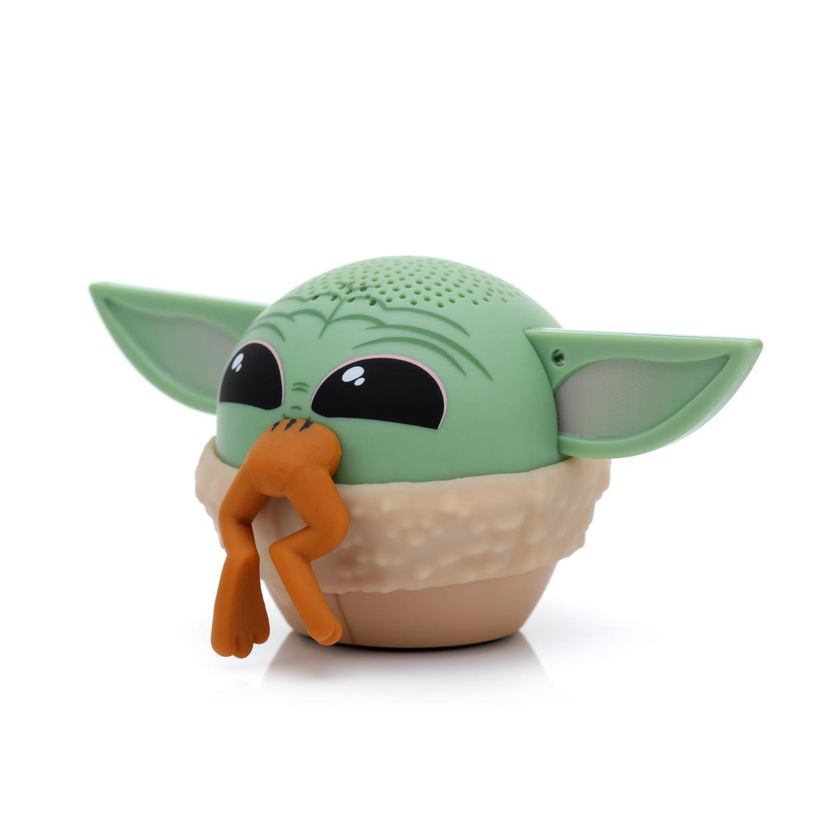 Büyük kulakları ve siyah gözleri olan yeşil bir Baby Yoda hoparlör oyuncağı. Turuncu bir nesne, muhtemelen bir kurbağa yiyor gibi görünüyor.
