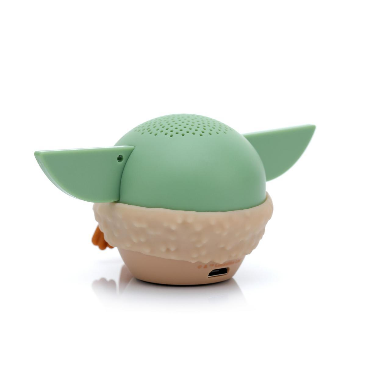 Yeşil bir Baby Yoda hoparlörü. Büyük kulakları, açık kahverengi bir tabanı ve bej bir yakası var. Hoparlörde bir USB bağlantı noktası var.