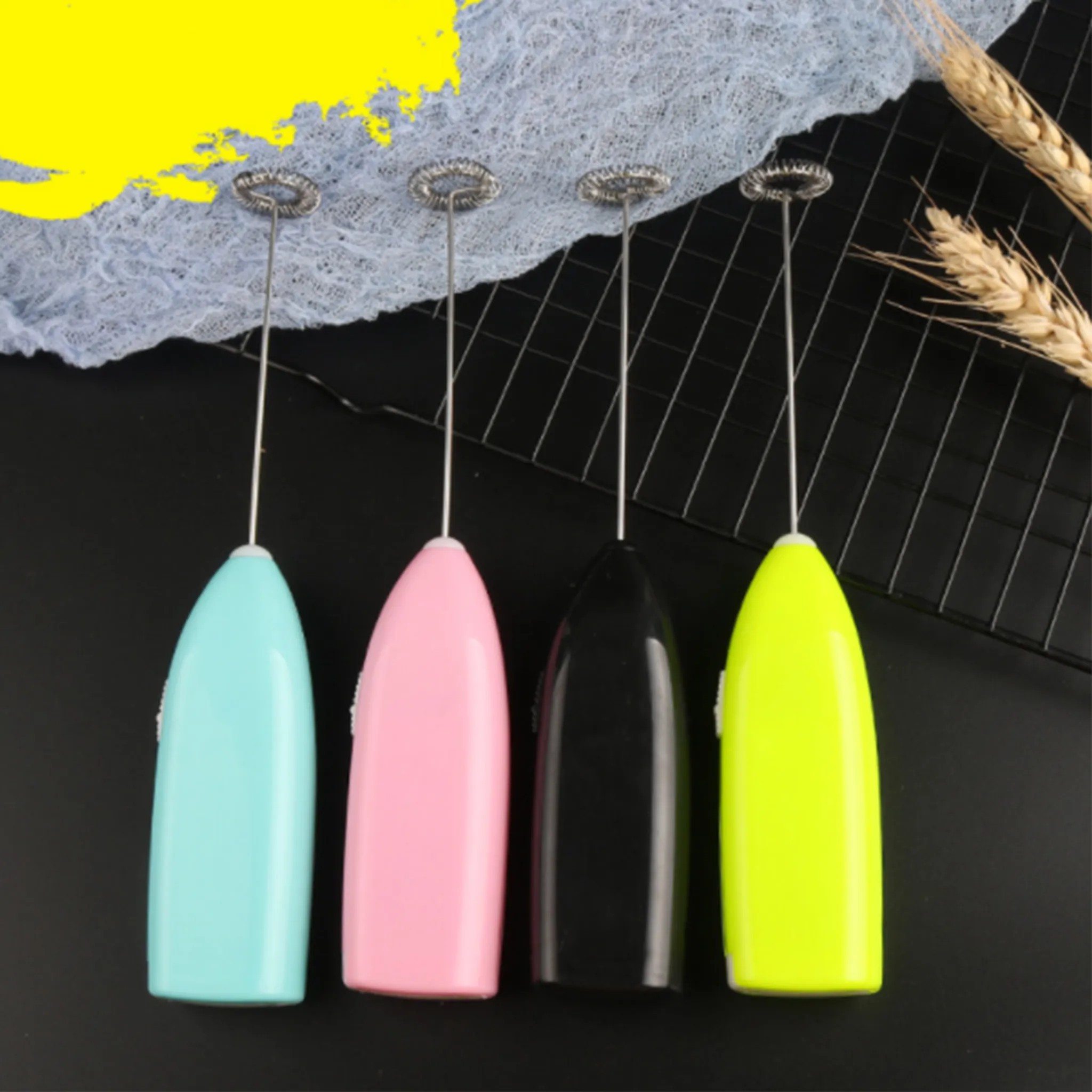Vier bunte Milchaufschäumer auf schwarzem Untergrund. Ein blauer, rosa, schwarzer und gelber sind in einer Reihe angeordnet.