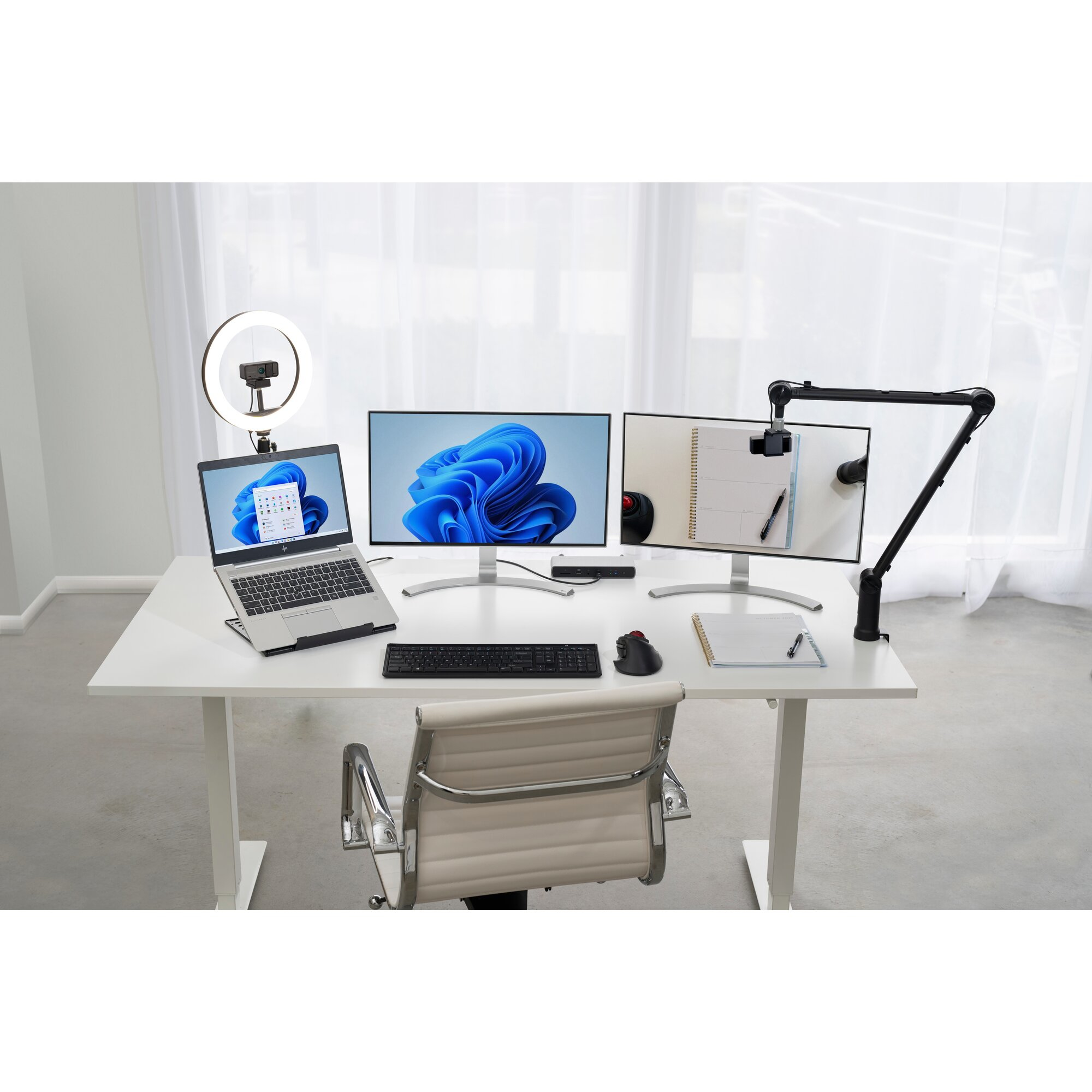 Nowoczesne miejsce pracy z laptopem, dwoma monitorami, klawiaturą, myszką, kamerą internetową, ringiem i krzesłem.