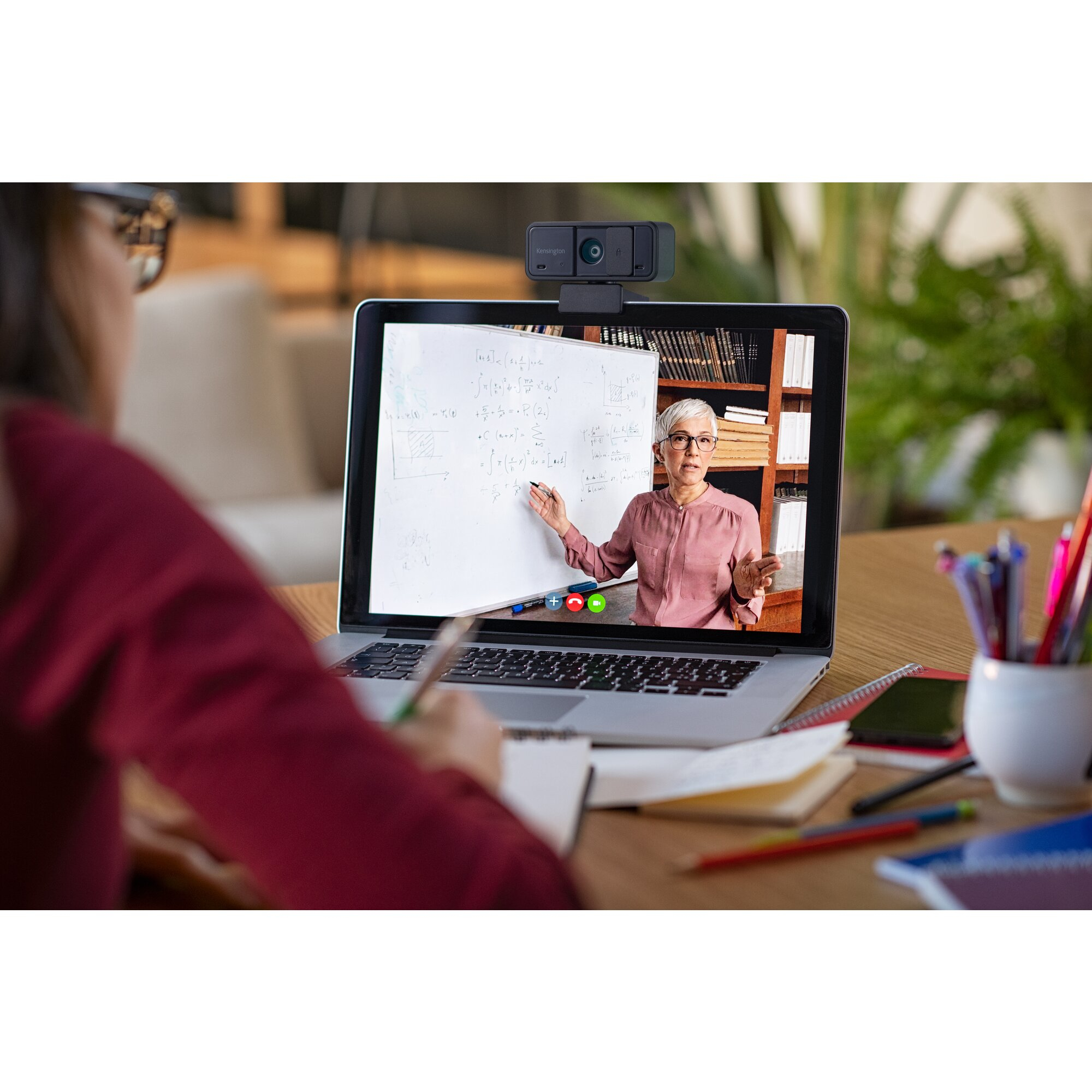 Osoba jest na rozmowie wideo. Na ekranie nauczyciel tłumaczy matematykę. Kamera internetowa znajduje się na górze laptopa.