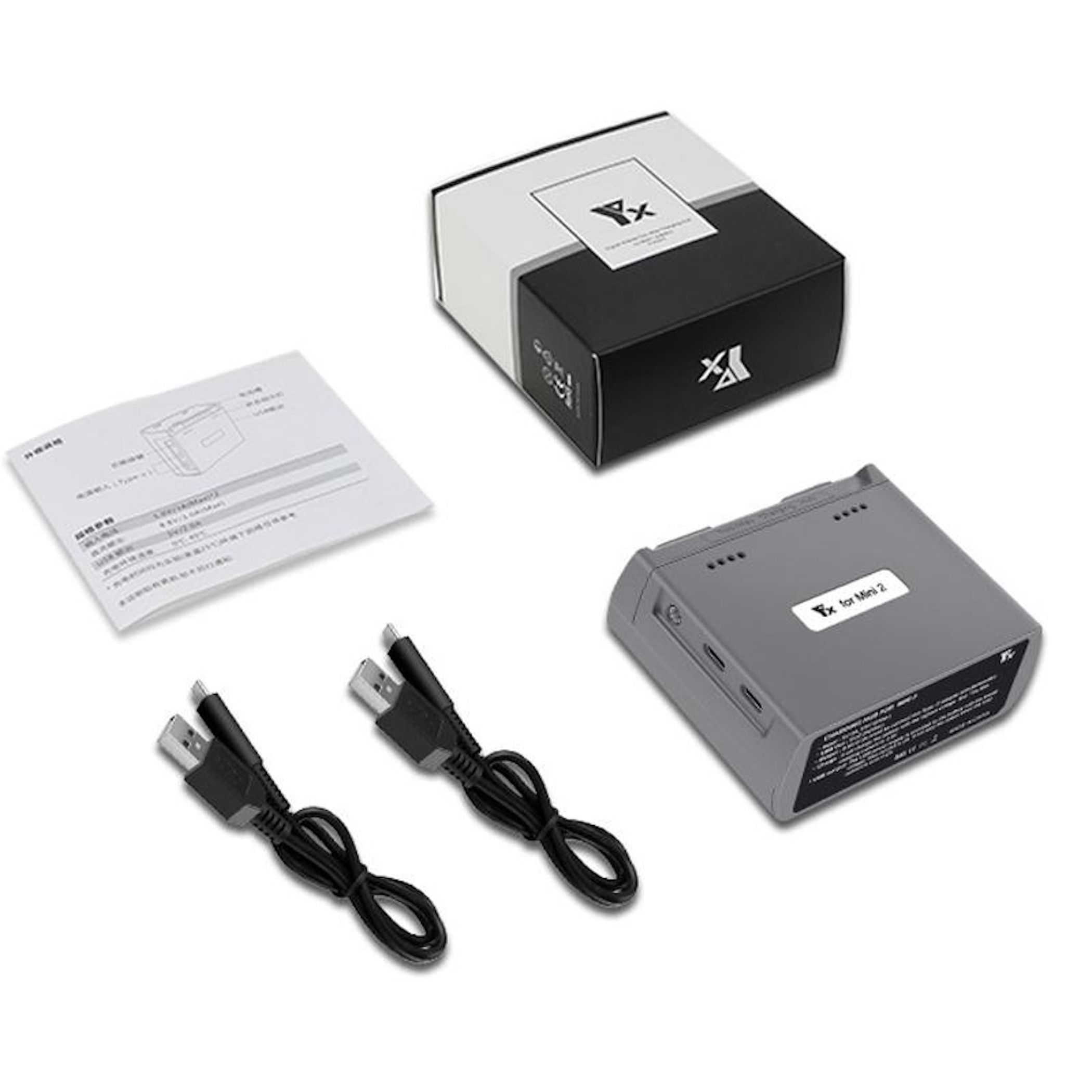 Eine graue Drohnenbatterie, eine schwarze Box, weißes Papier und zwei USB-Kabel liegen auf einer weißen Oberfläche.