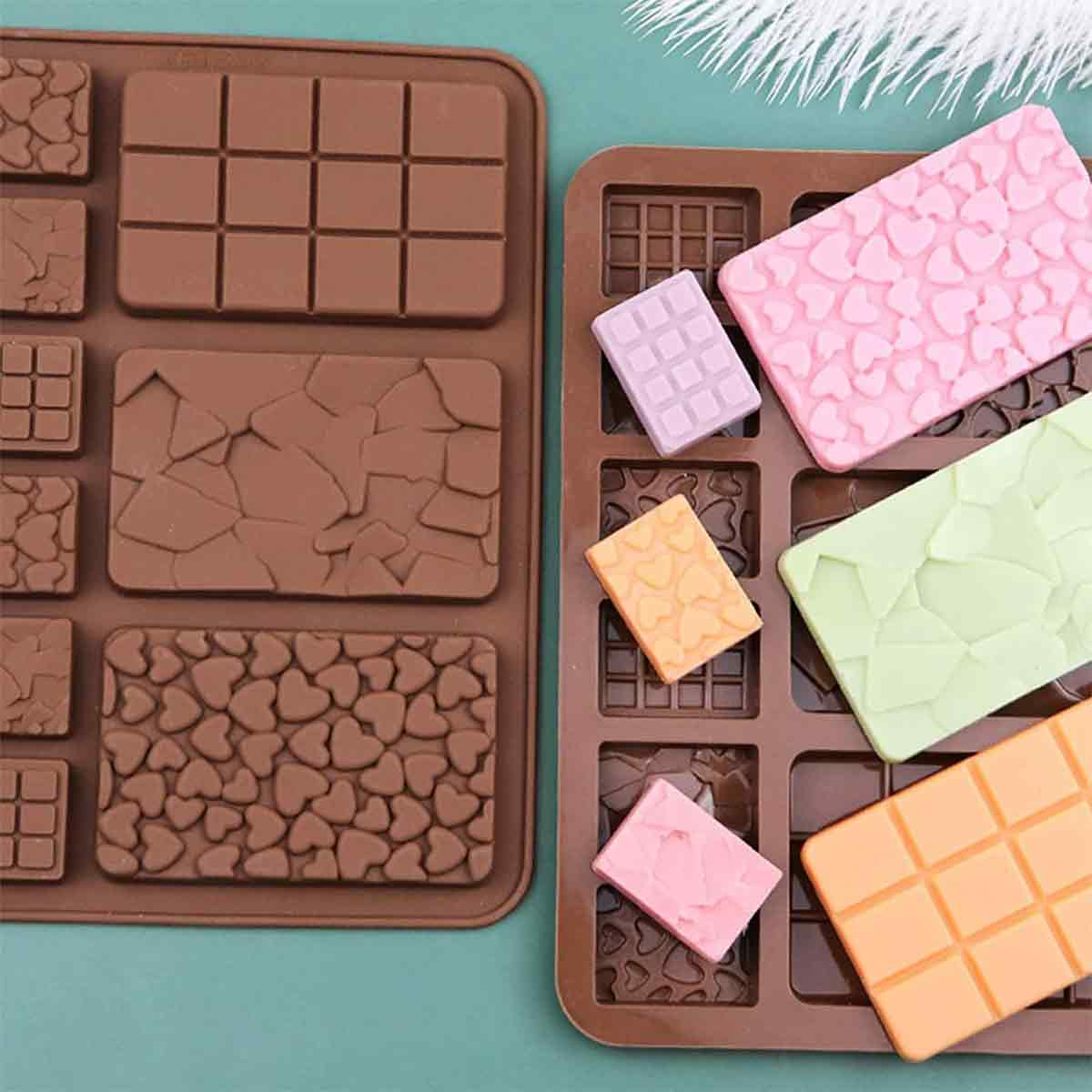 Zwei Tabletts mit Schokoladenformen. Eines hat braune Formen, das andere enthält rosa, grüne, orange und lila Pralinen.