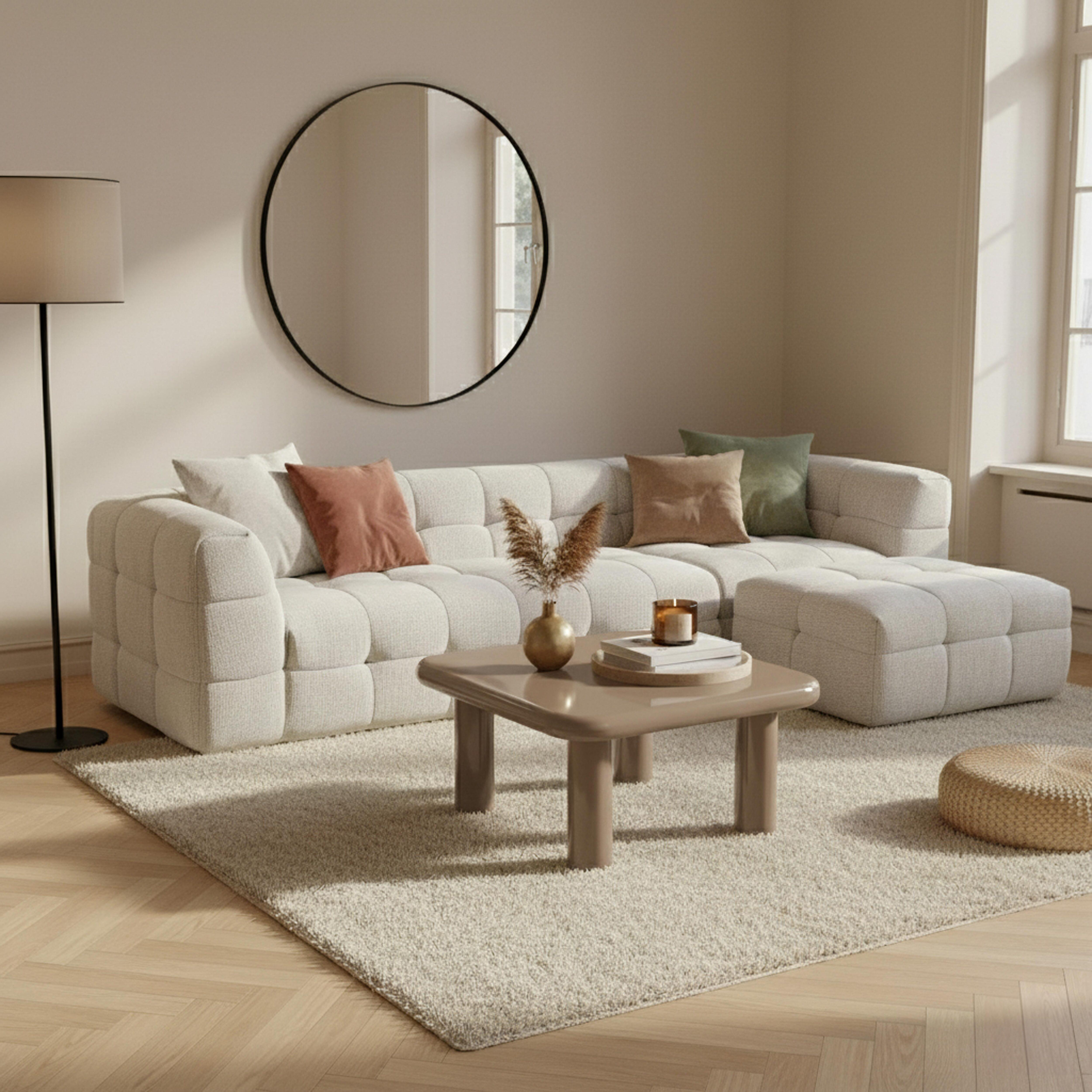 Modernes Wohnzimmer mit weißem Sofa, rundem Spiegel, Couchtisch und Teppich. Sanfte, neutrale Töne schaffen Ruhe.