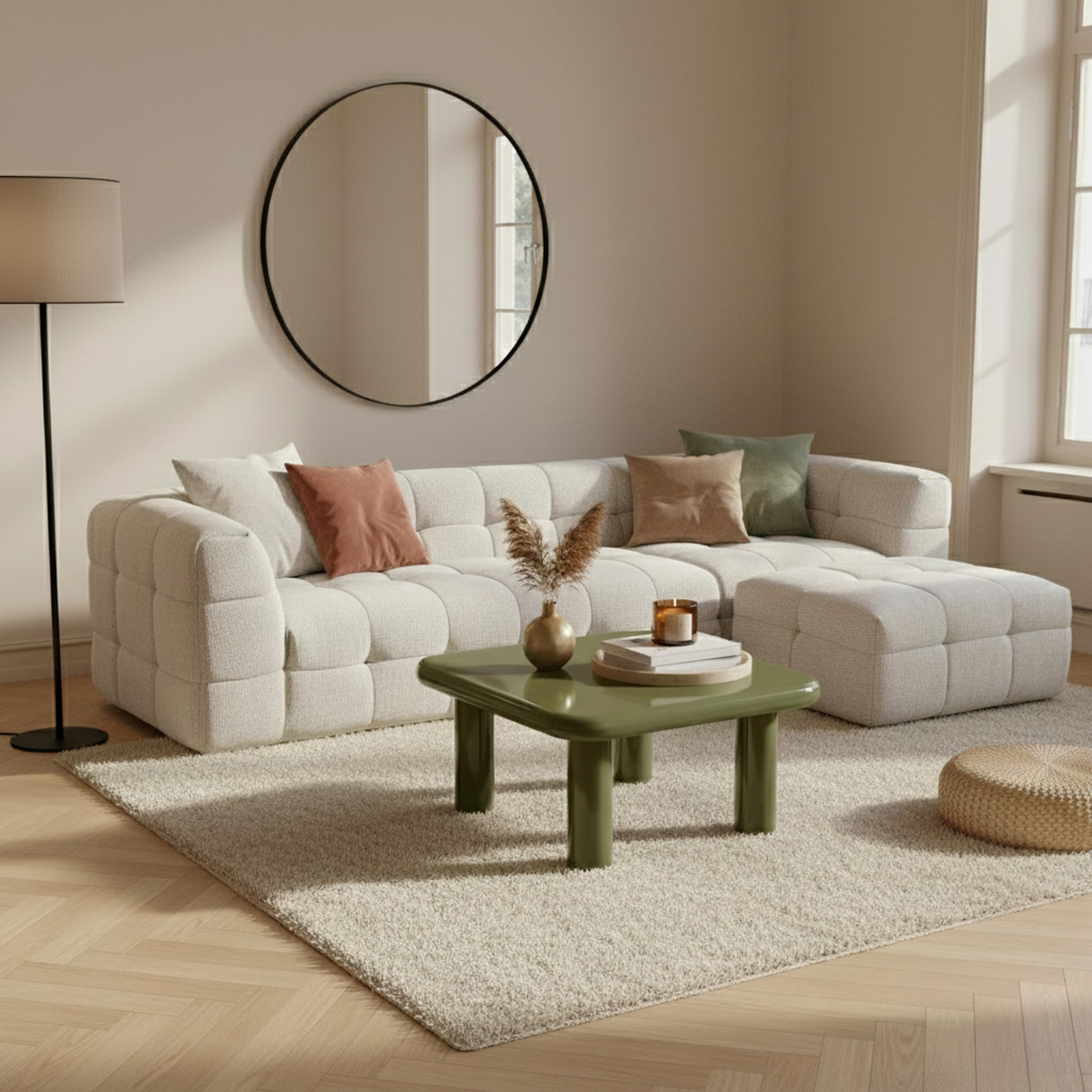 Modernes Wohnzimmer mit weißem Sofa, grünem Tisch, Teppich, Spiegel und Lampe. Der Raum hat neutrale Farben.