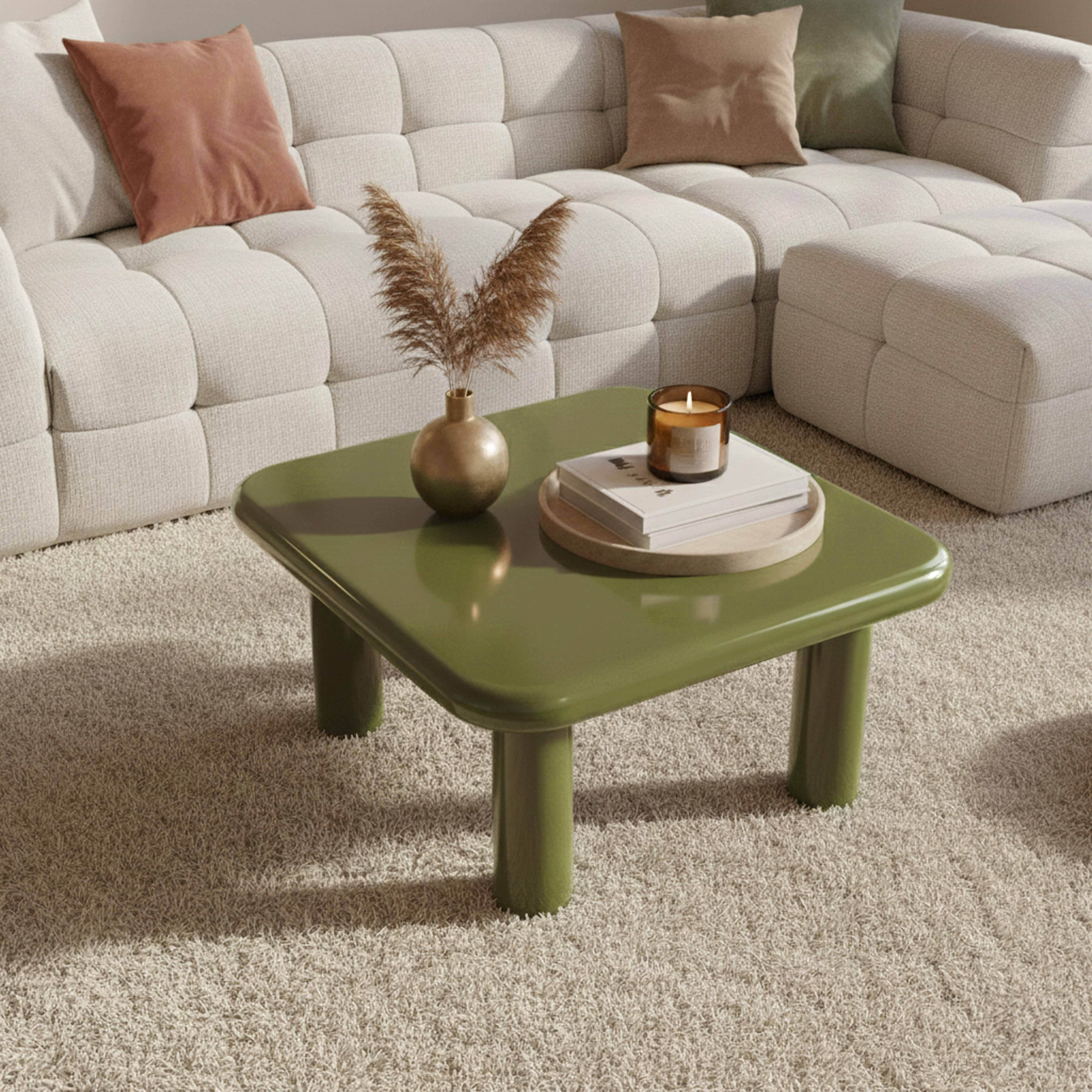 Ein grüner Couchtisch mit einer Vase und einer Kerze steht auf einem hellen Teppich vor einem weißen Sofa mit Kissen.