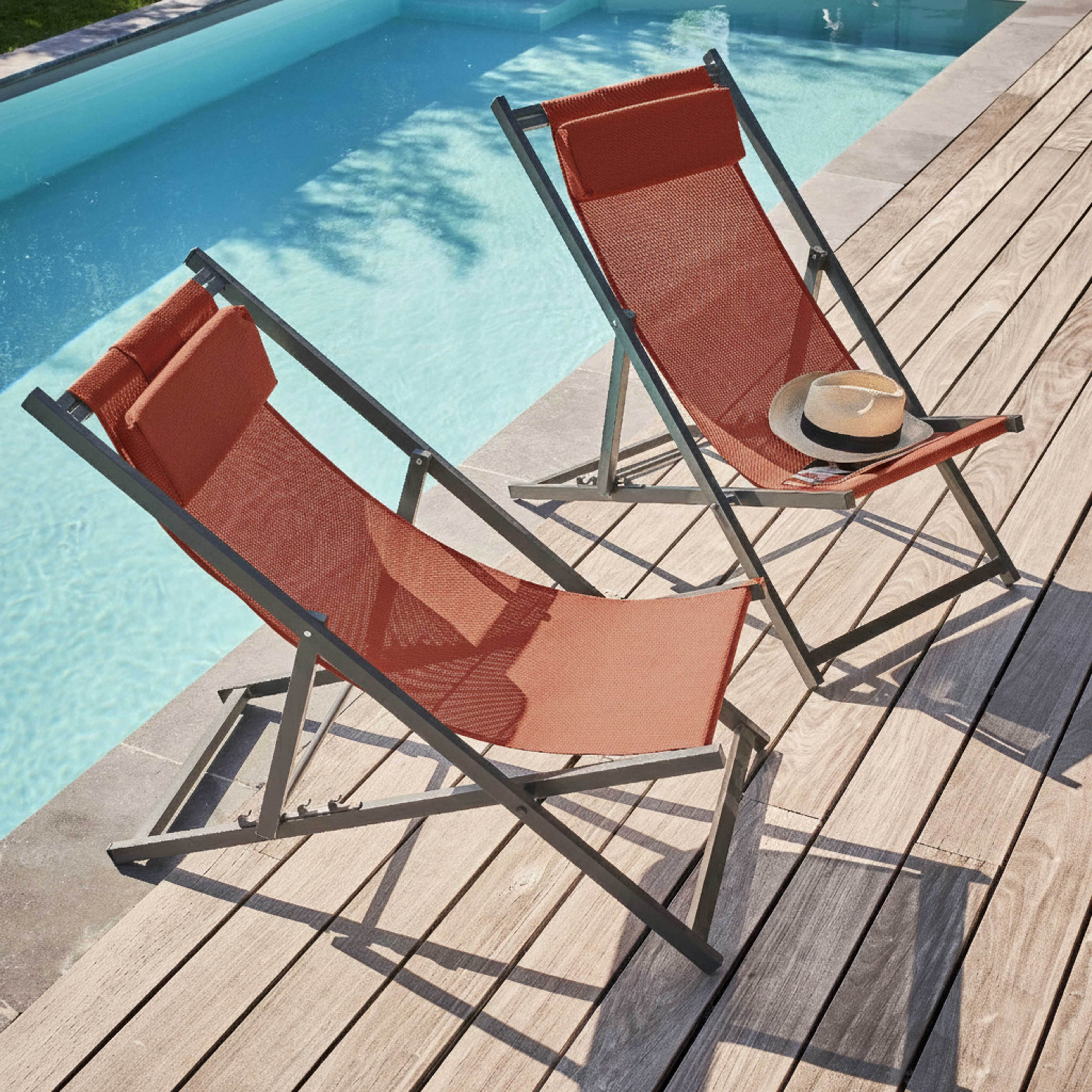 Zwei orangefarbene Liegestühle auf Holzdeck am Pool. Ein Hut liegt auf einem Stuhl.