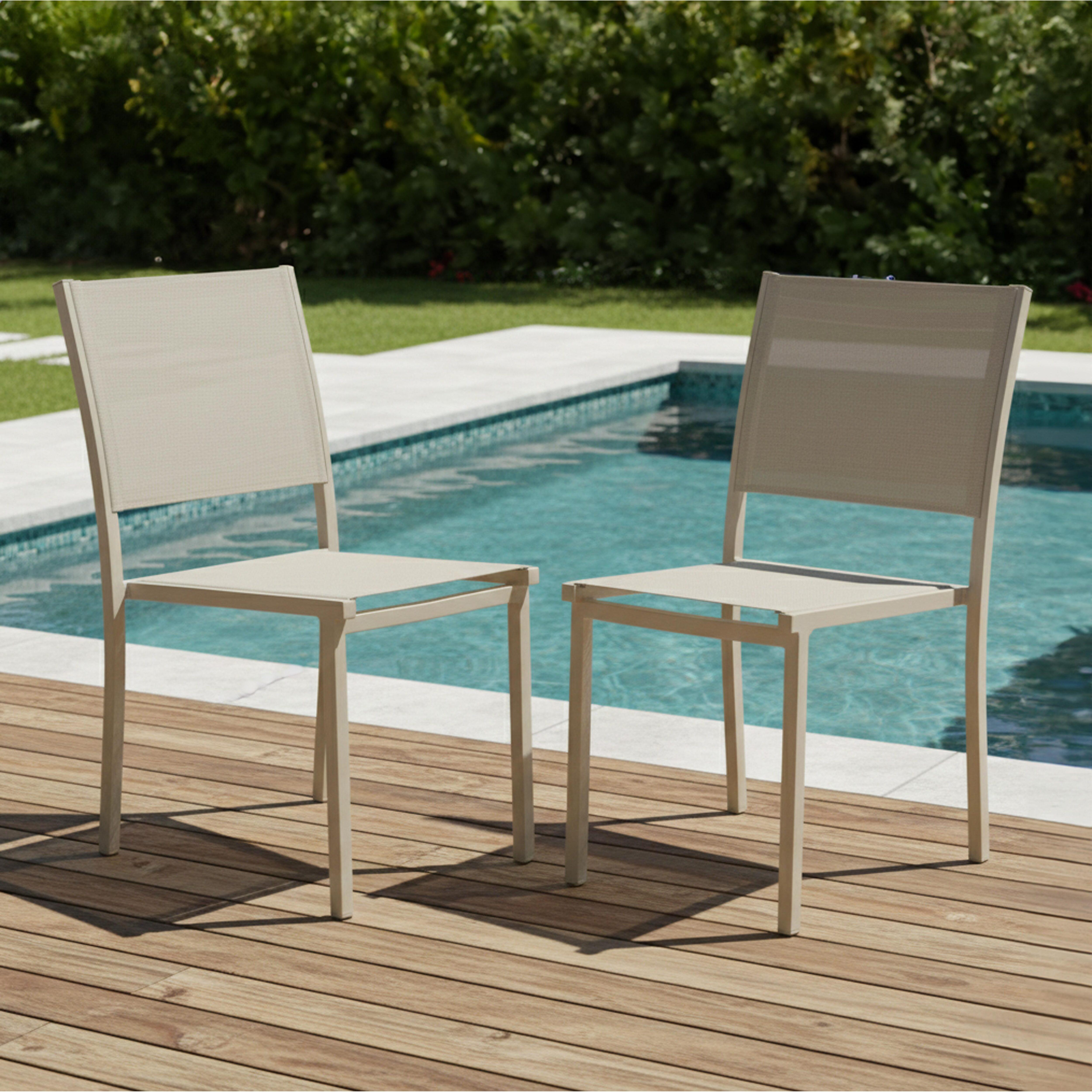 Zwei beige Stühle stehen auf Holzbohlen am Pool. Grüne Büsche sind im Hintergrund. Das Wasser ist blau.