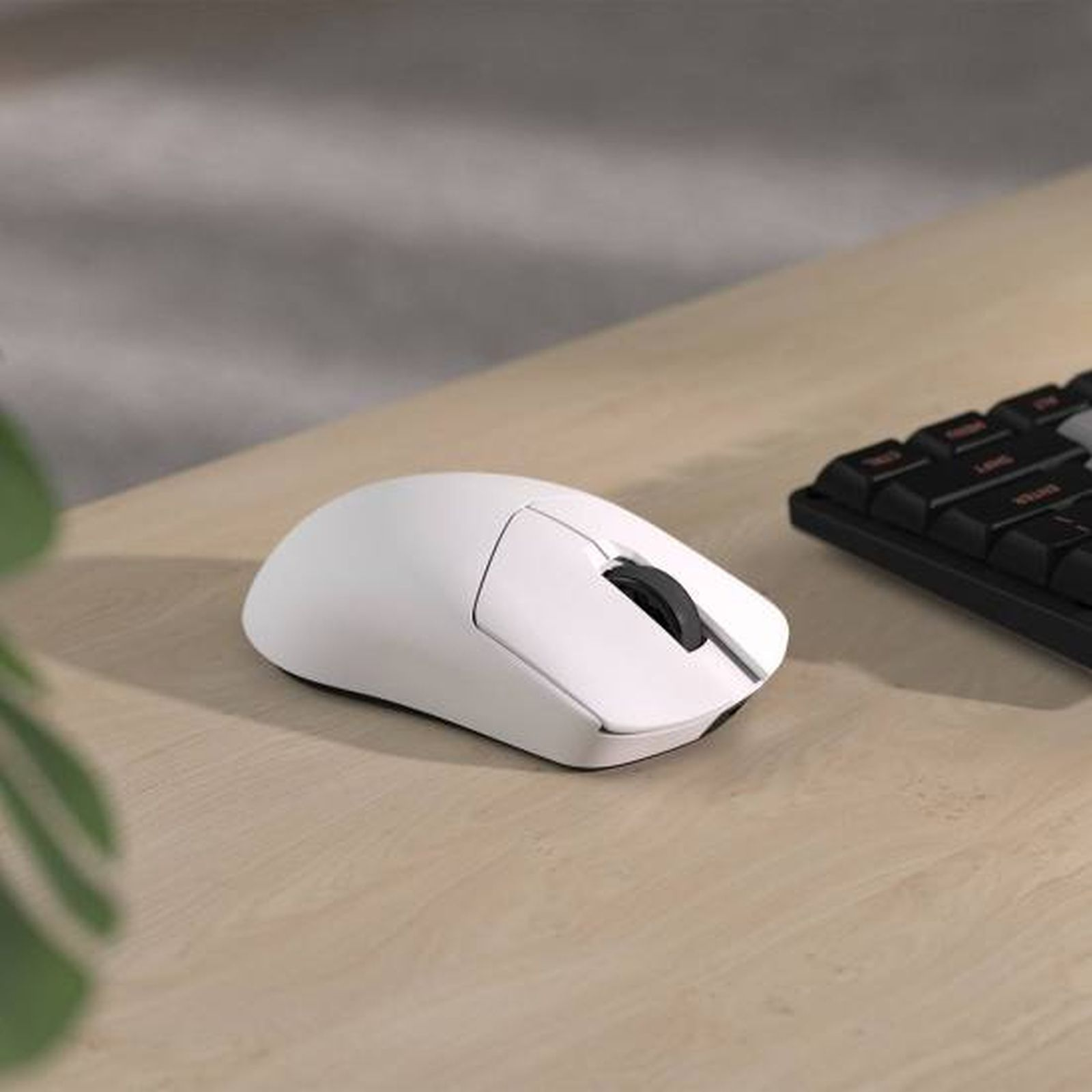 Un mouse bianco con rotella nera e una tastiera nera sono su una scrivania di legno.