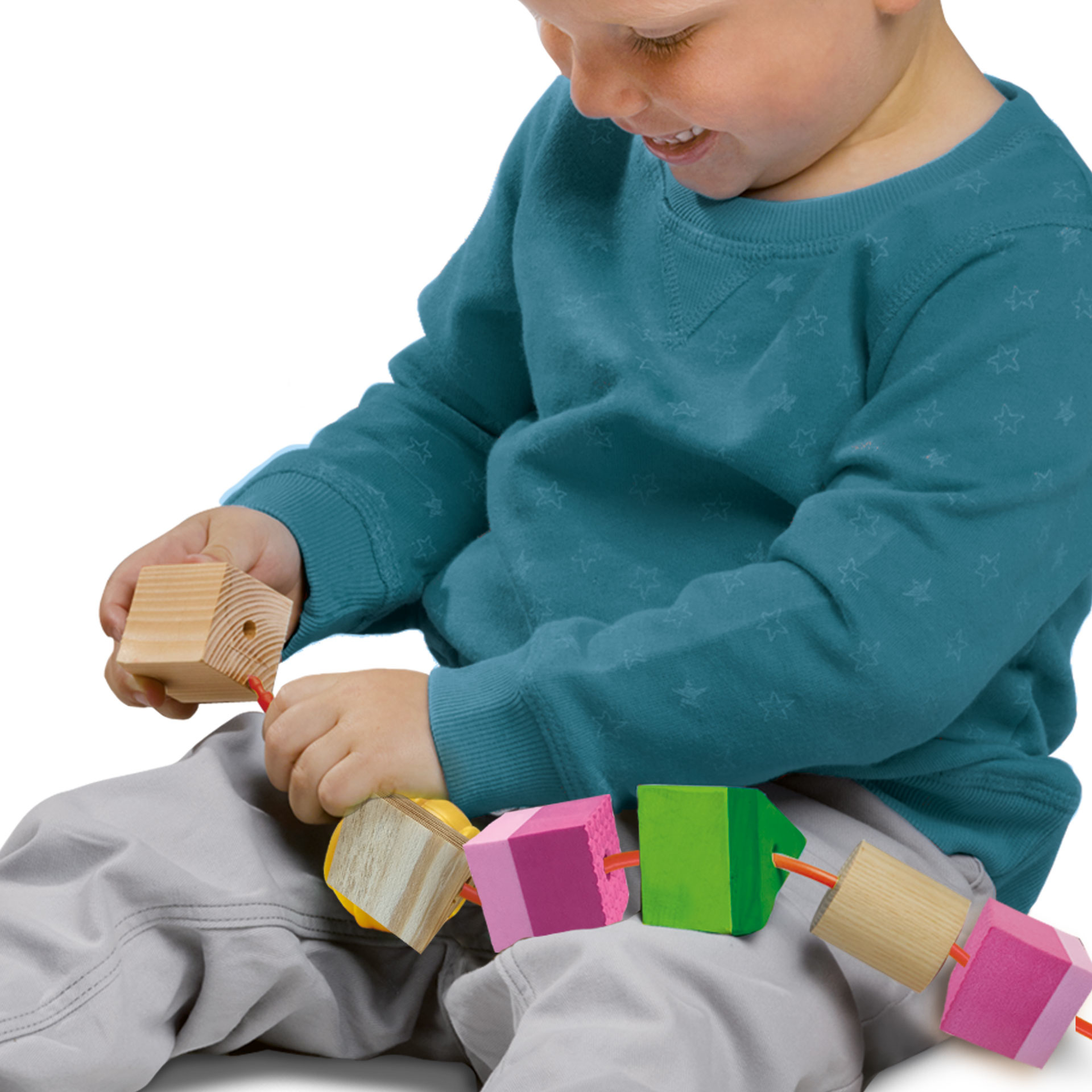 Un niño juega con bloques de madera de colores en una cuerda. El niño lleva un suéter azul y pantalones grises.