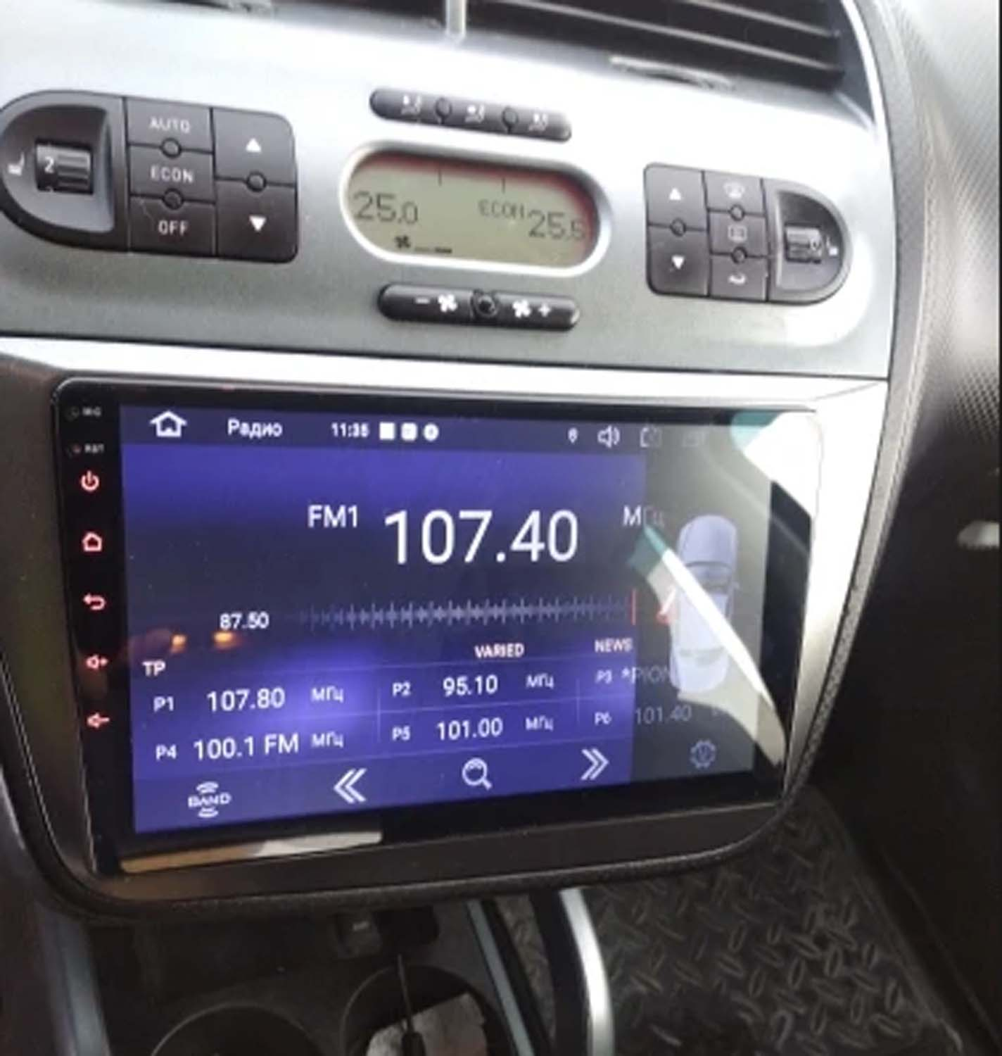 Panel del coche mostrando radio en 107.40 FM, rodeado de botones y pantallas. Controles de clima arriba.