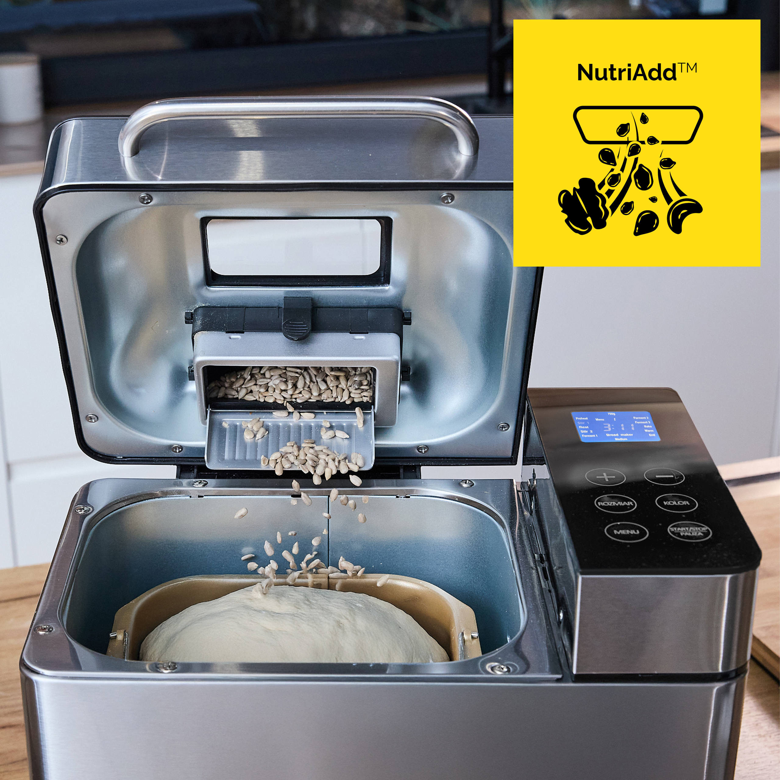 Maszyna do pieczenia chleba z nasionami słonecznika dodawanymi do ciasta. Widoczny panel sterowania i logo NutriAdd.
