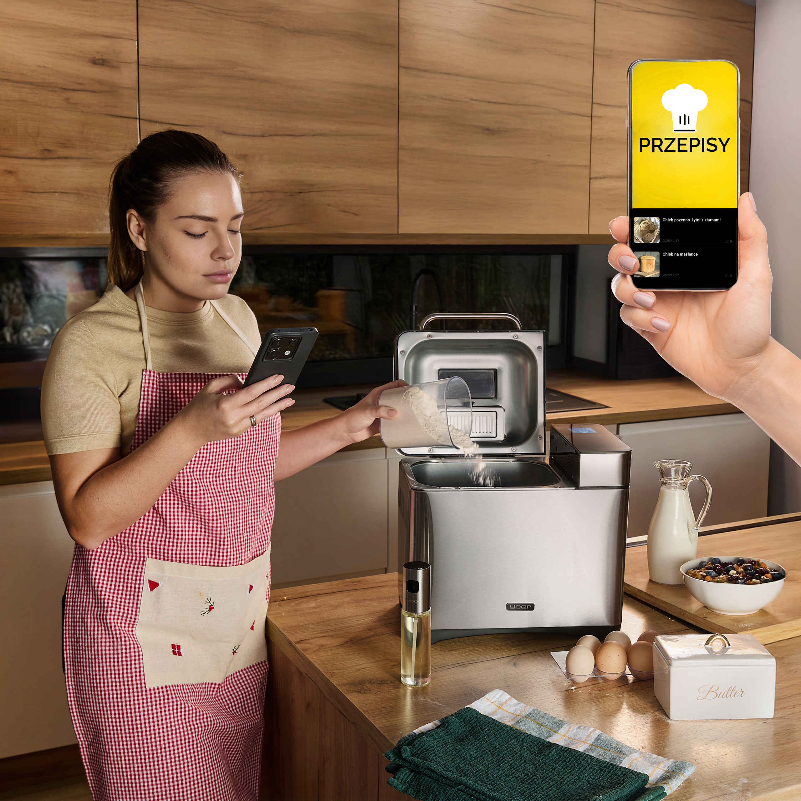 Kobieta w kuchni, używa telefonu do przepisów, dodaje mąkę do wypiekacza chleba. Składniki i masło na blacie.
