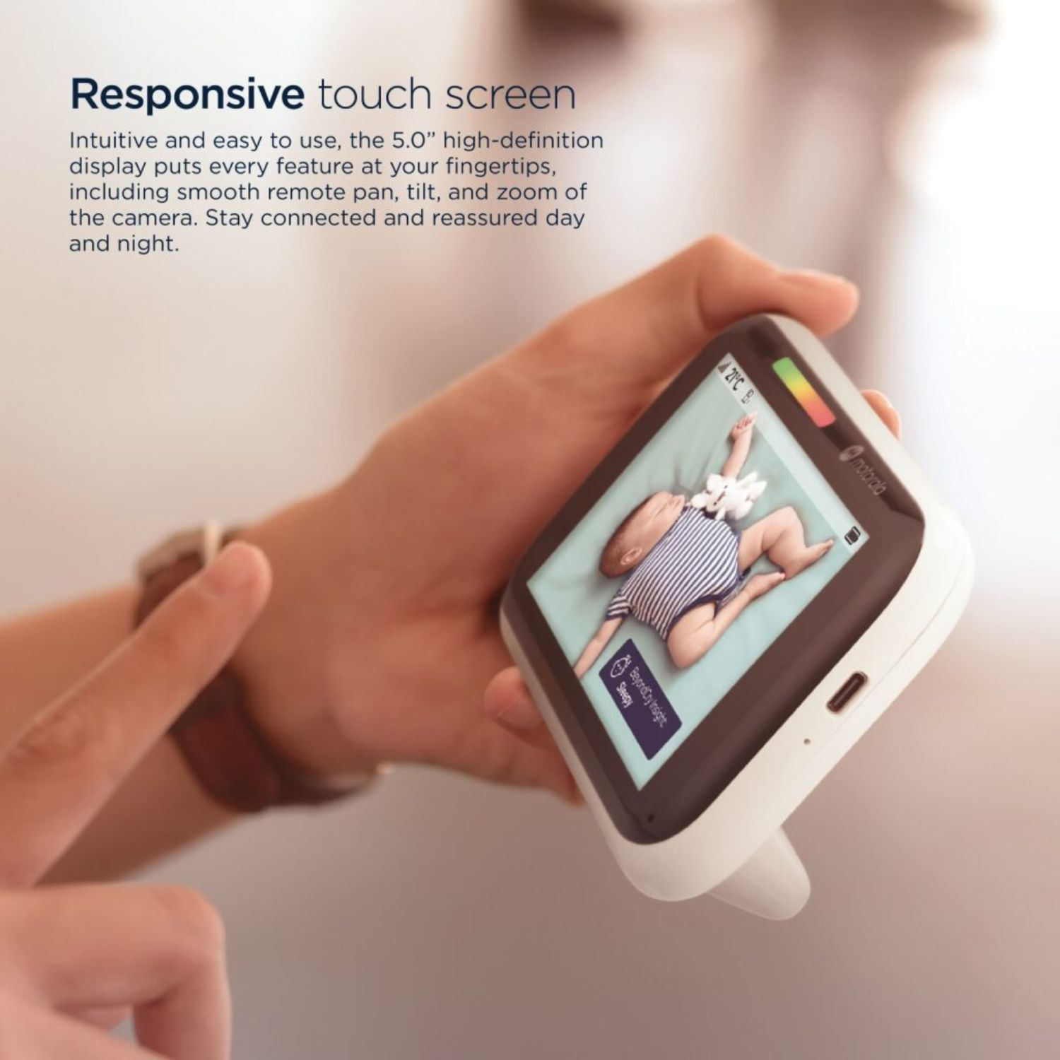 Eine Person hält einen Babyphone, das ein Baby zeigt. Der Monitor zeigt das schlafende Baby. Der Monitor ist weiß und hat einen Touchscreen.