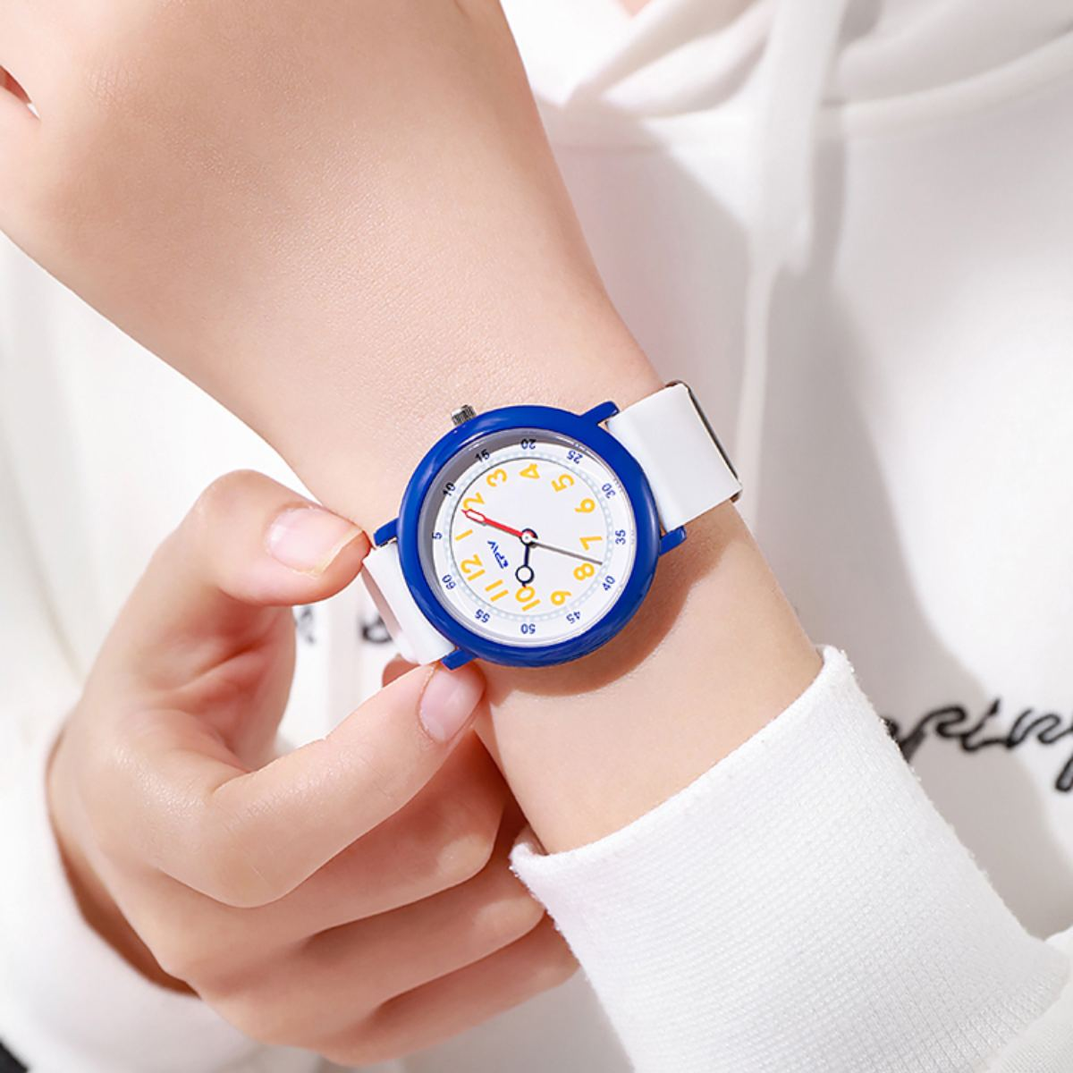 Muñeca de una persona con un reloj blanco y azul. El reloj tiene un bisel azul, una correa blanca y números coloridos en la esfera.