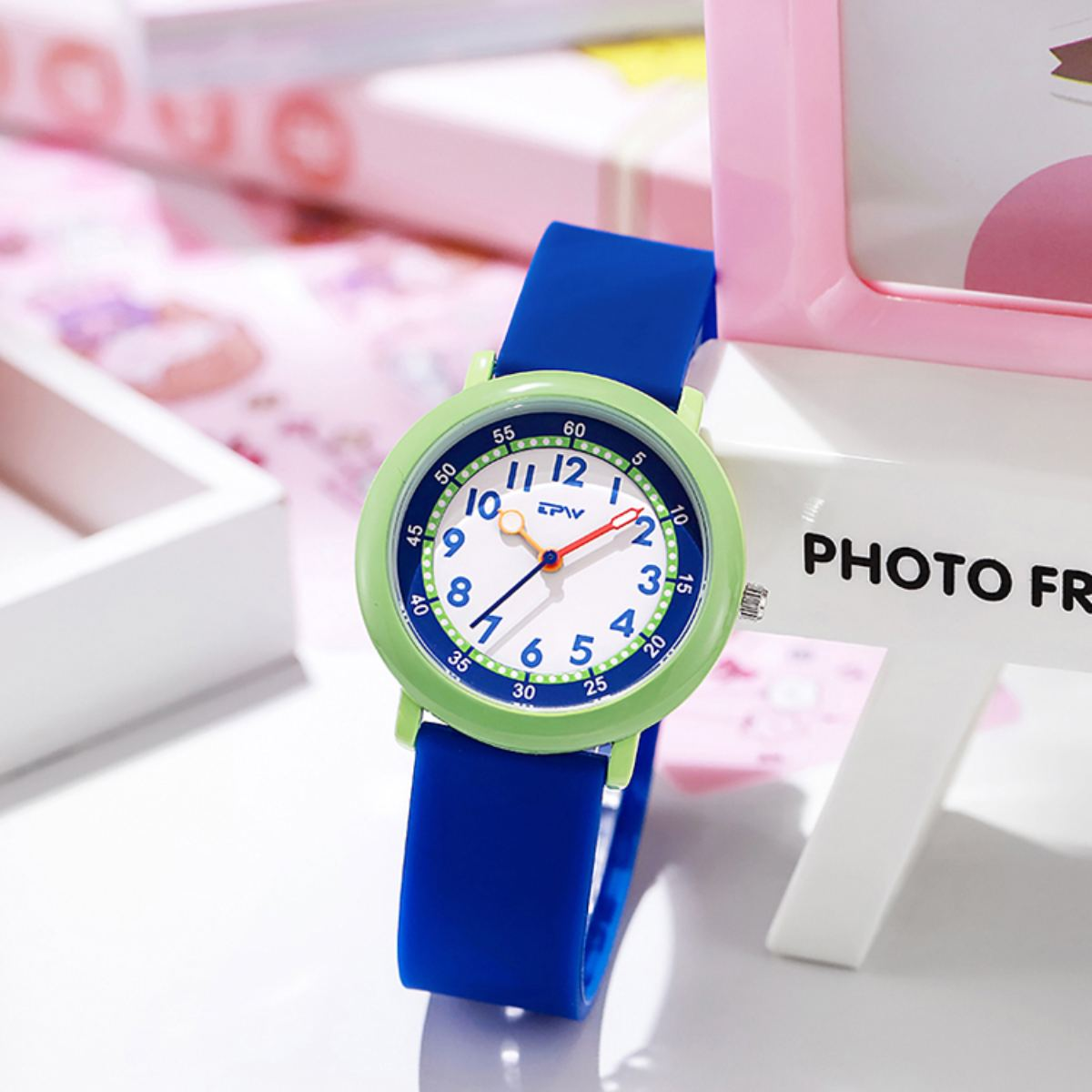 Nahaufnahme einer Kinderuhr mit blauem Armband und grüner Lünette. Das Zifferblatt ist weiß mit schwarzen Ziffern und roten Zeigern.
