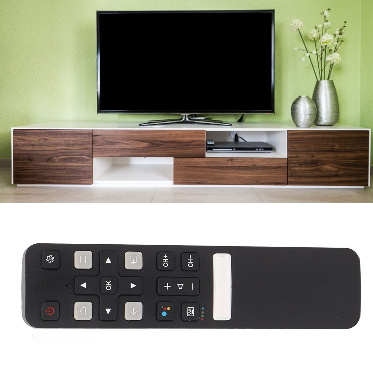Ein Fernseher steht auf einem weiß-braunen Schrank. Eine Fernbedienung ist im Vordergrund. Vasen mit Blumen sind rechts.