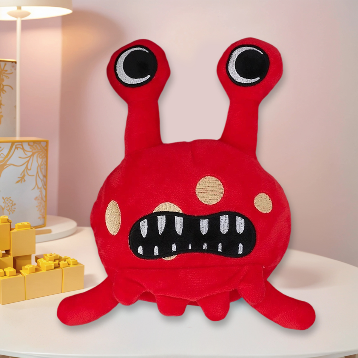 Ein rotes Plüschmonster mit großen Augen und Zähnen sitzt auf einem weißen Tisch. Links sind gelbe Bausteine.