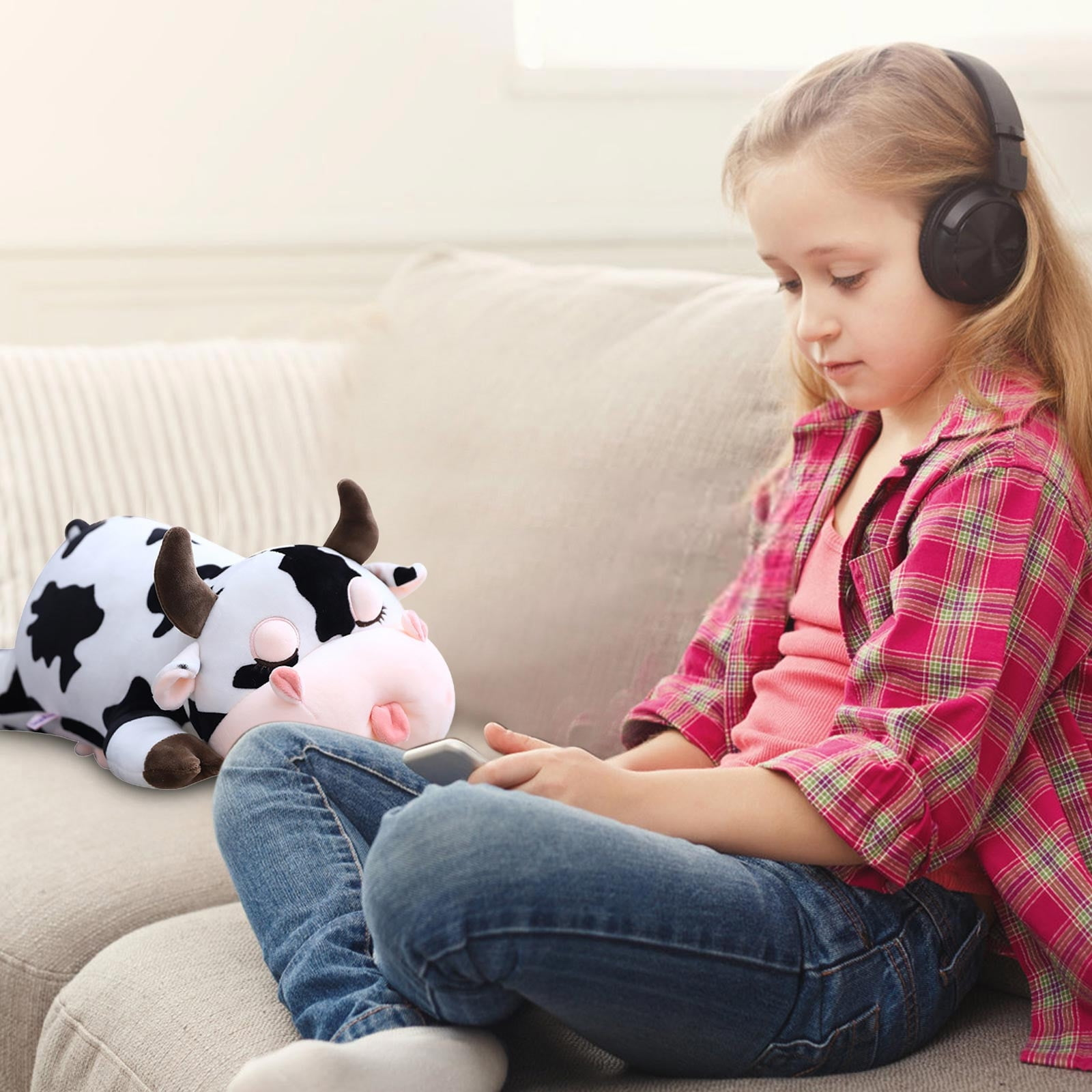 Ein Mädchen mit Kopfhörern benutzt ein Telefon, ein Kuhplüschtier liegt neben ihm auf einem Sofa.