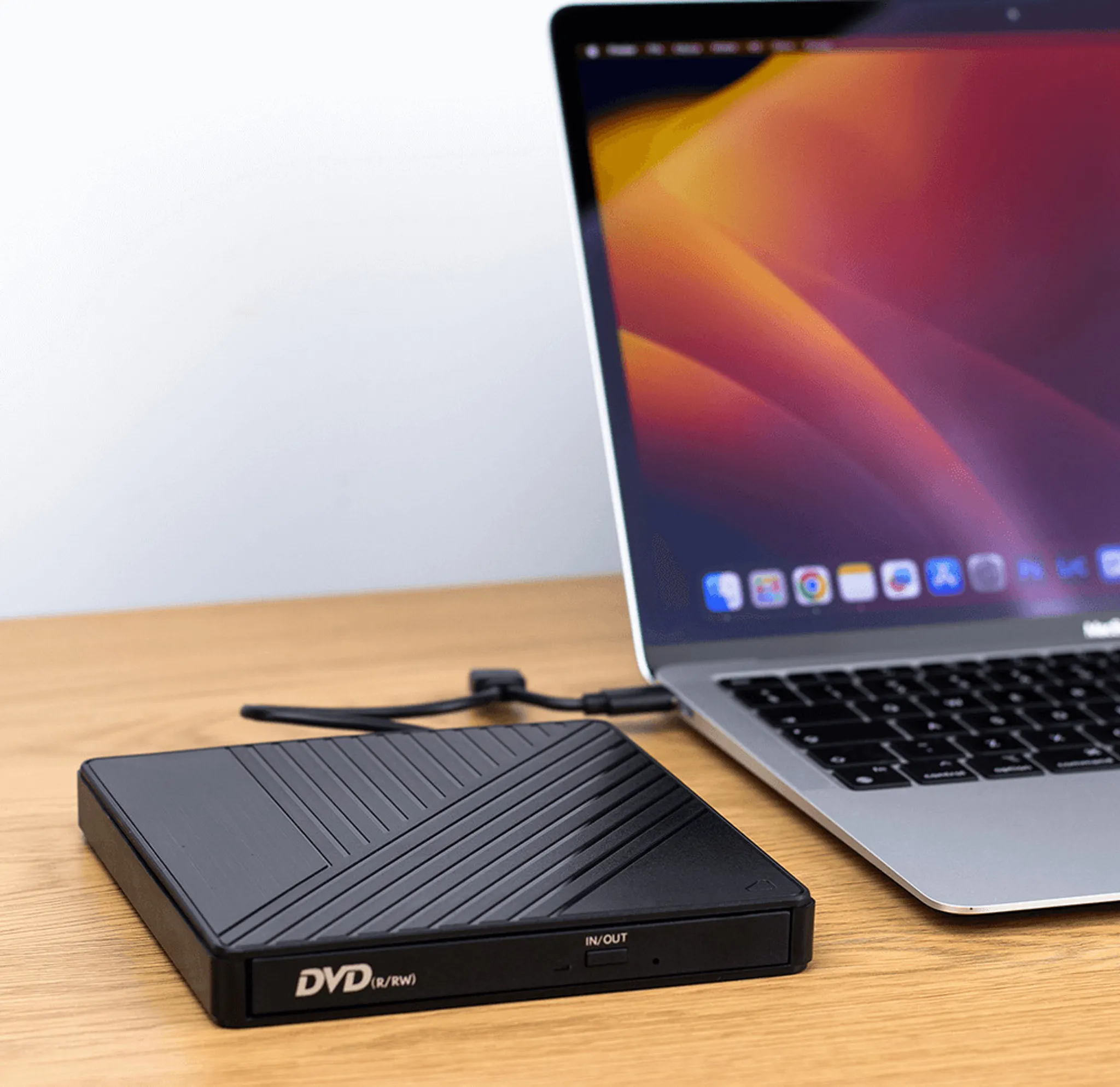 Ein Laptop mit einem schwarzen DVD-Laufwerk steht auf einem Holztisch. Der Laptop ist geöffnet, und das DVD-Laufwerk ist angeschlossen.
