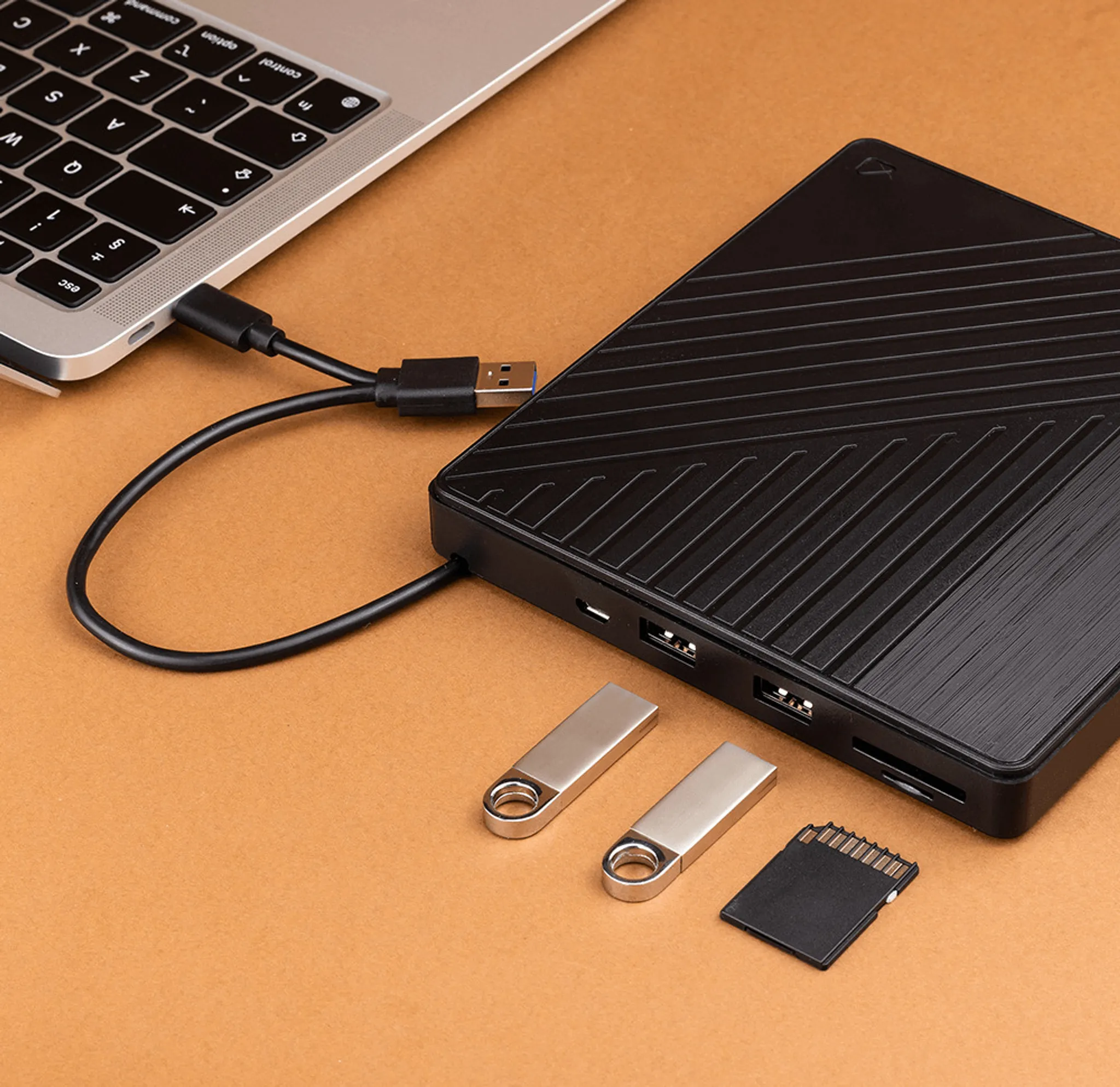 Ein Laptop, verbunden mit einem schwarzen Hub, mit USB-Laufwerken und einer SD-Karte auf orangefarbener Oberfläche.