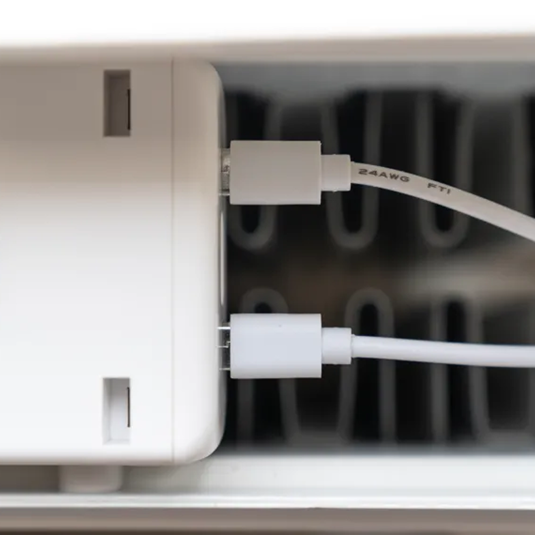 Close-up van een witte oplaadblok met twee witte USB-C-kabels. Een radiator op de achtergrond.