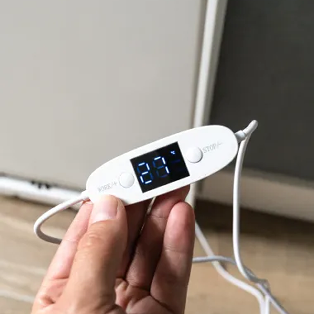 Een hand houdt een witte digitale thermometer vast met 29 graden. Het apparaat heeft knoppen en een kabel, met een vage achtergrond.