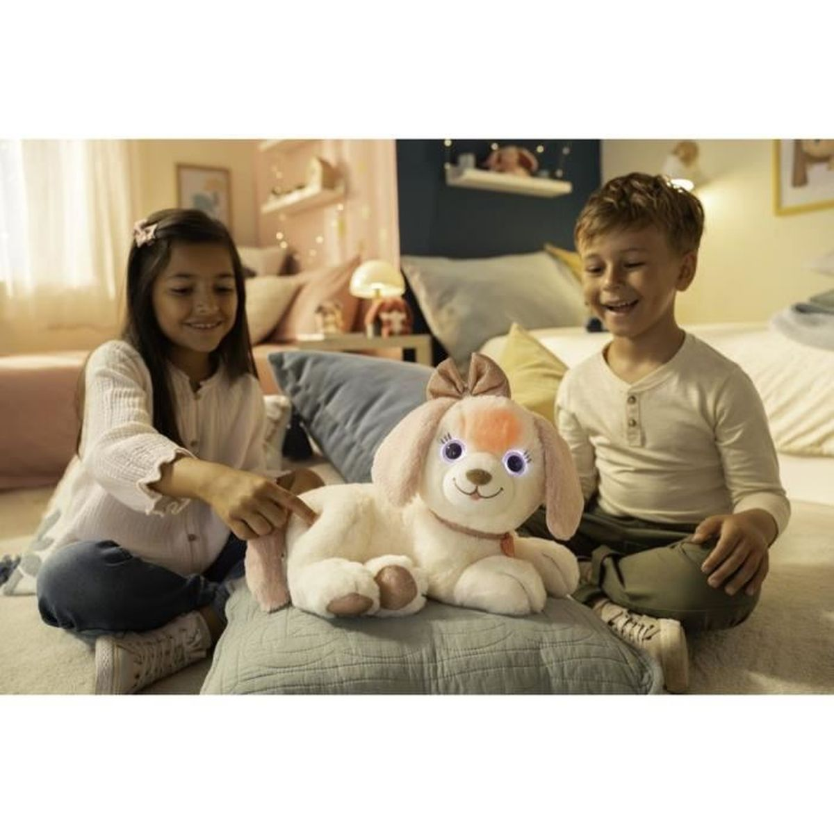 Deux enfants sourient à un chien en peluche avec un nœud. Le jouet a des yeux brillants. Ils sont assis sur un lit.