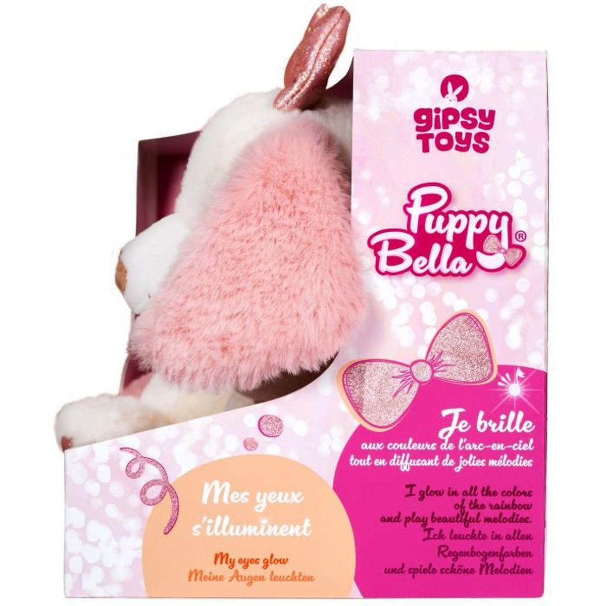 Une peluche Puppy Bella dans une boîte rose. Le jouet est blanc et rose. Le texte dit 'Mes yeux s'illuminent' et 'Je brille'.