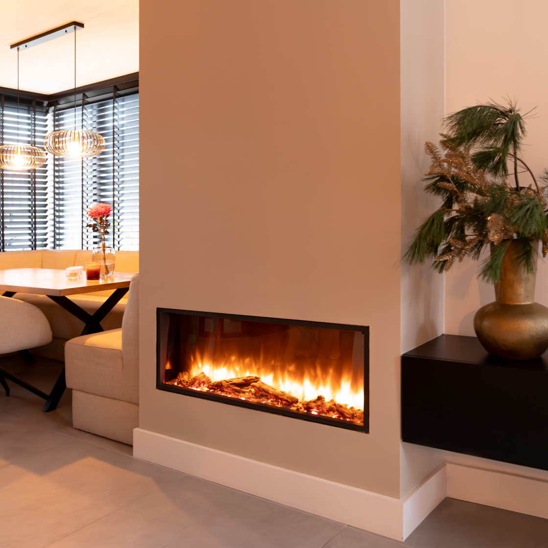Een moderne woonkamer met een open haard, een tafel en een vaas met planten. De open haard staat aan en de lichten zijn aan.
