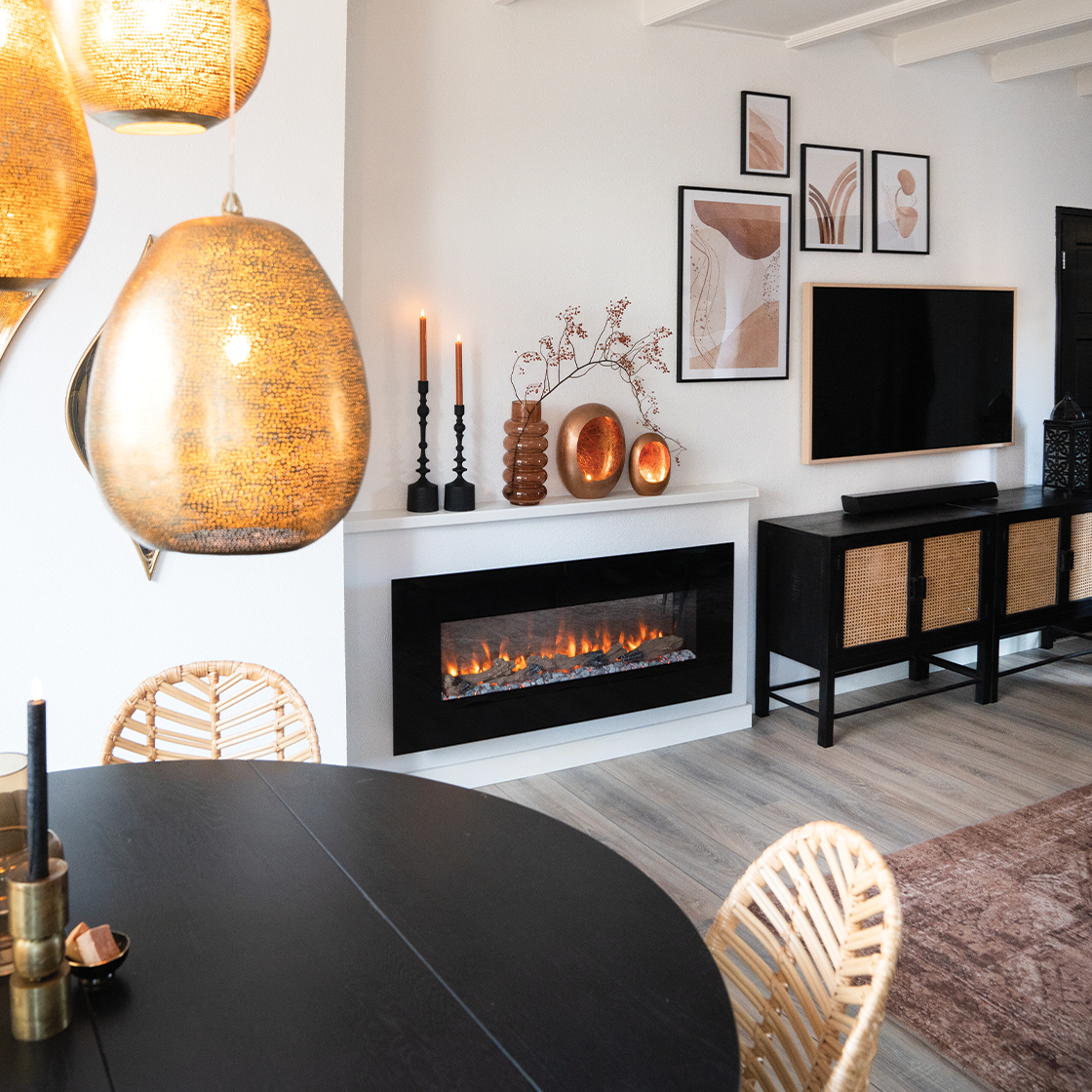 Een moderne woonkamer met open haard, tv en zwarte tafel. Decoratieve lampen hangen aan het plafond. Rotan stoelen omringen de tafel.