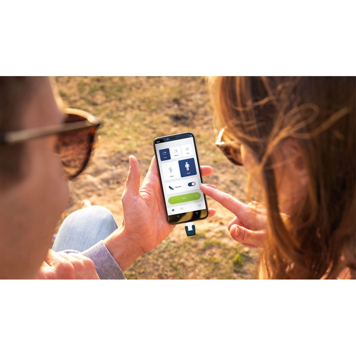 Dos personas usan un smartphone. La pantalla muestra una aplicación con opciones. Una persona señala la pantalla.