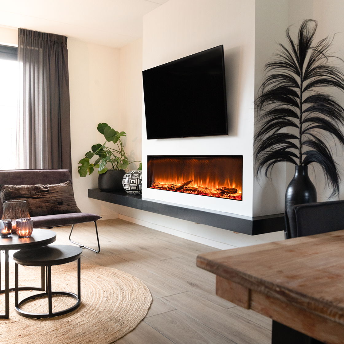 Woonkamer met een tv, open haard en planten. Een stoel, salontafels en een houten tafel. De kamer heeft houten vloeren.