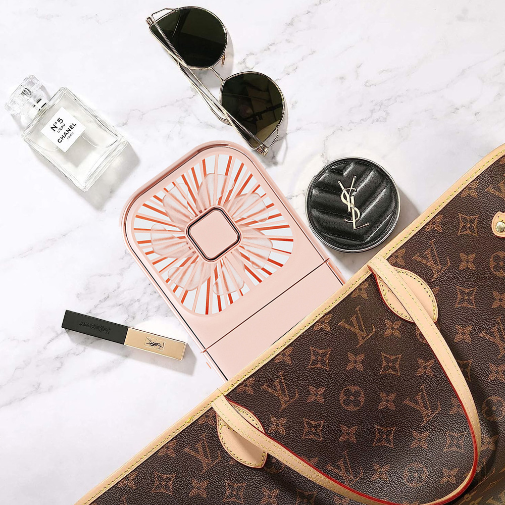 Draufsicht auf eine Tasche, Sonnenbrille, Ventilator, Parfüm, Make-up und Kompaktpuder auf Marmor.