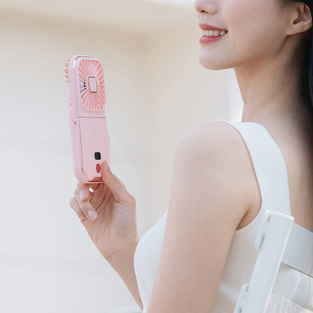 Eine Frau hält einen rosa Handventilator. Sie lächelt und trägt ein weißes Kleid. Der Ventilator ist geöffnet und läuft.
