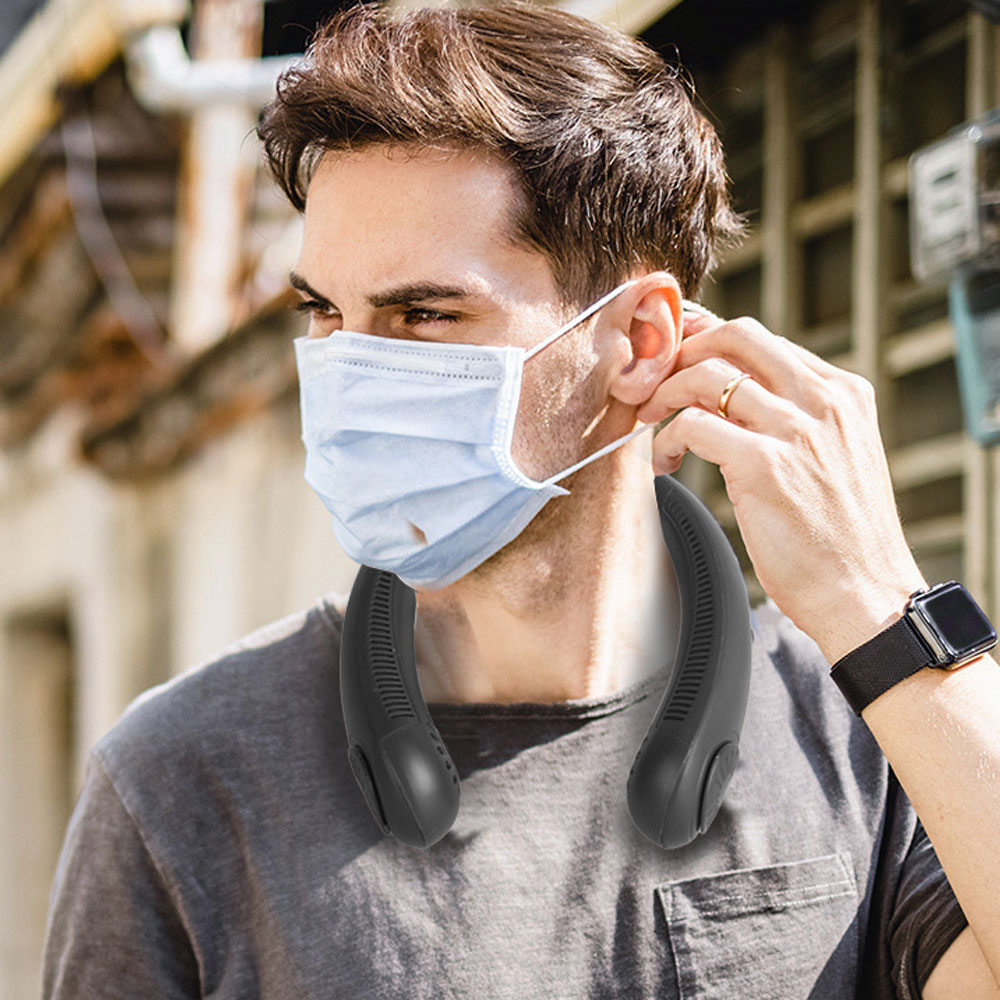Ein Mann mit Maske und Nackenfächer. Er passt seine Maske an. Er trägt eine Uhr und einen Ring. Hintergrund ist ein Gebäude.
