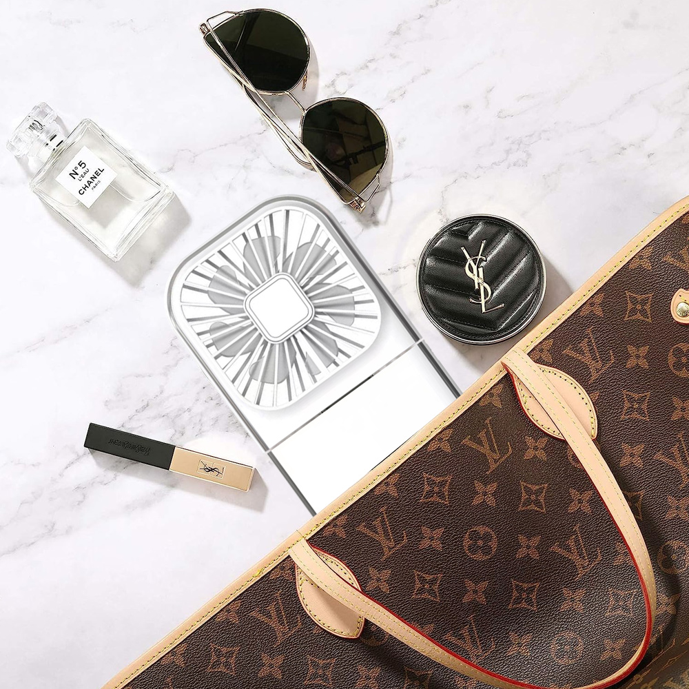 Draufsicht auf Sonnenbrille, Parfüm, Ventilator, Make-up, Geldbörse und Kompaktpuder auf Marmor. Die Geldbörse ist von Louis Vuitton.